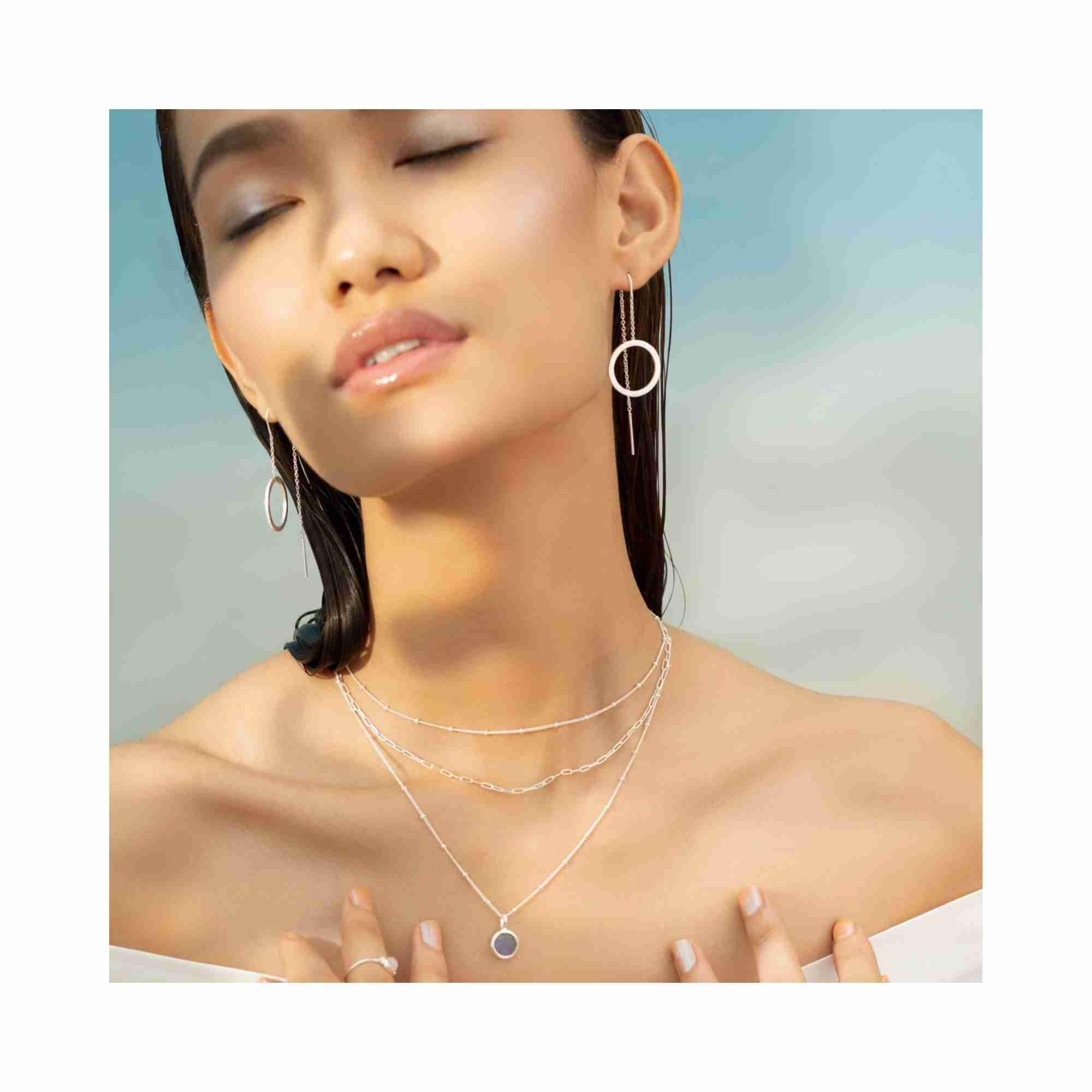 Detail shot of a model wearing the Shimmering Disks silver circle chain threader earrings, demonstrating how the lightweight silver disks catch the light for a modern, everyday luxury look — Protsaah Zurich.