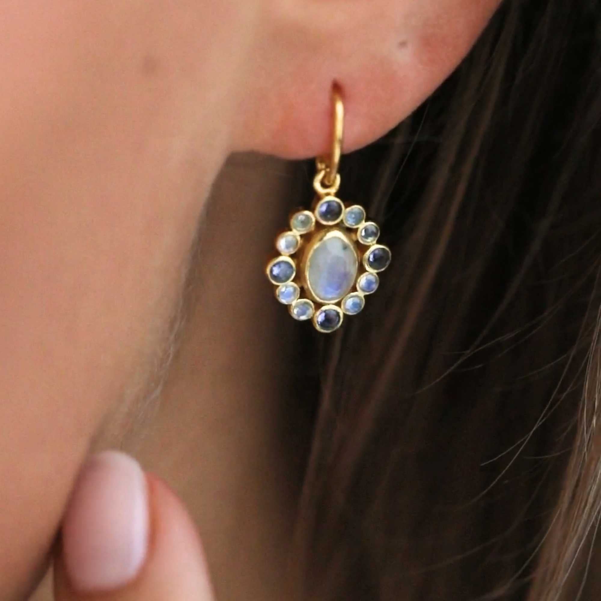 Delicate Vintage Halo Cluster Moonstone & Iolite Drop Earrings Gold — close-up lifestyle shot of a model wearing a 22K gold-plated sterling silver drop earring, showcasing the iridescent blue flash of the oval-cut natural Rainbow Moonstone and its scalloped halo cluster of round iolite and moonstone gemstones — Protsaah.