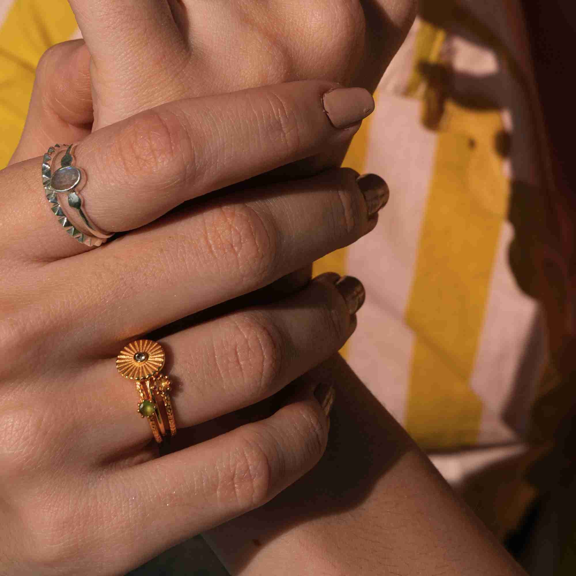 A close-up view of a model's hands with a beige manicure, showcasing a mixed metal ring stack featuring a silver gemstone ring alongside the Delicate Vintage Nephrite Jade Fluted Disc Ring in Gold by Protsaah Zurich.