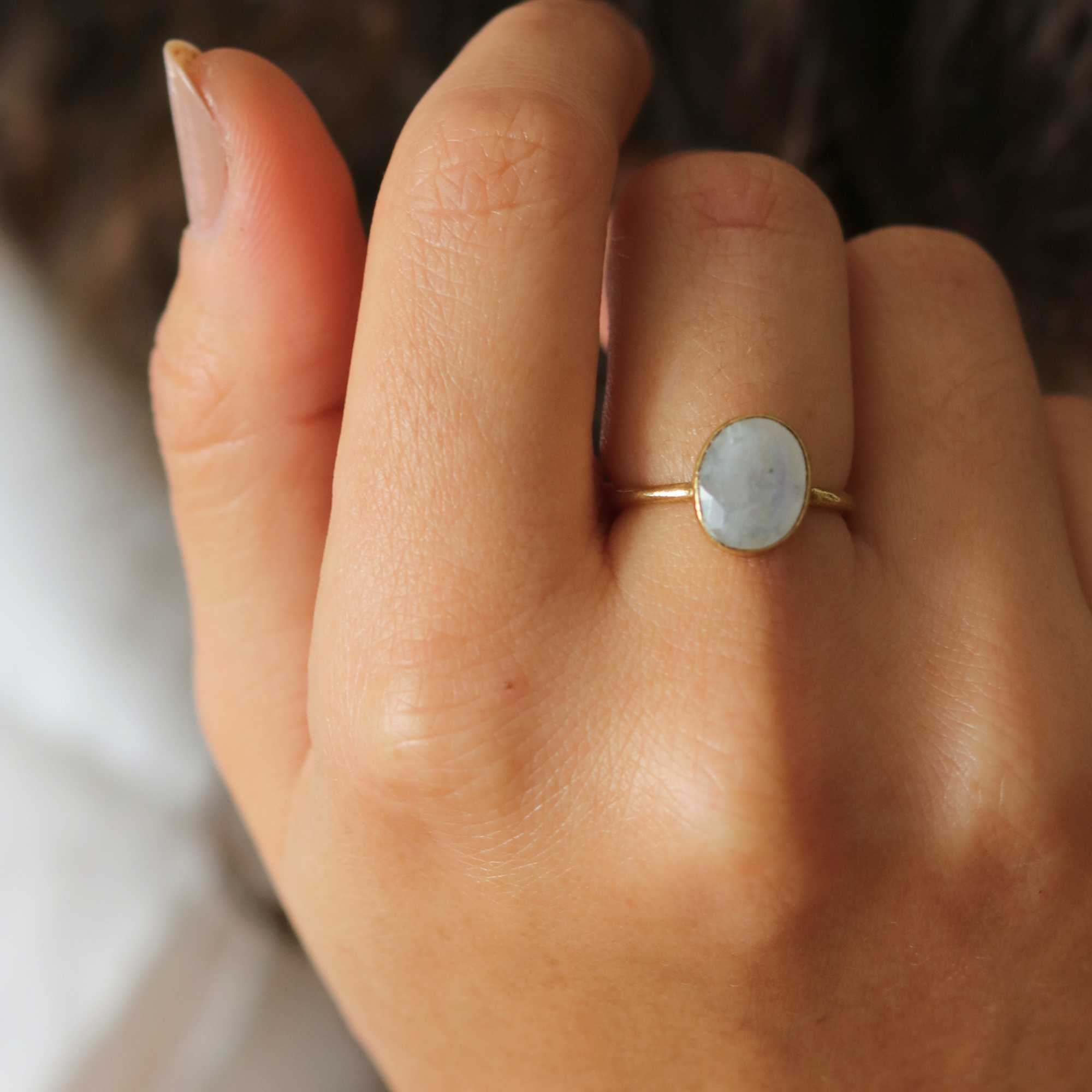 A model showcasing the Dew Drops Oval Aqua Chalcedony Adjustable Ring in gold, featuring a vibrant, bezel-set oval aqua chalcedony gemstone centered on a minimalist textured gold band, styled alongside other delicate stacking rings.