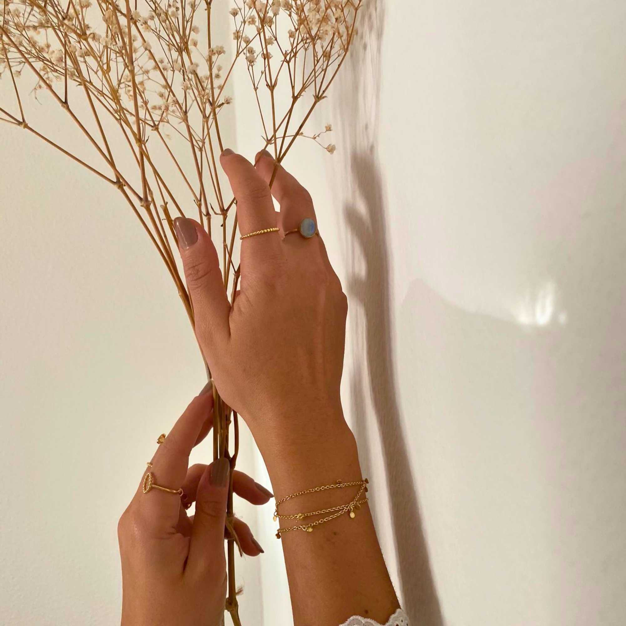 A model showcasing the Dew Drops Oval Aqua Chalcedony Adjustable Ring in gold, featuring a vibrant, bezel-set oval aqua chalcedony gemstone centered on a minimalist textured gold band, styled alongside other delicate stacking rings.