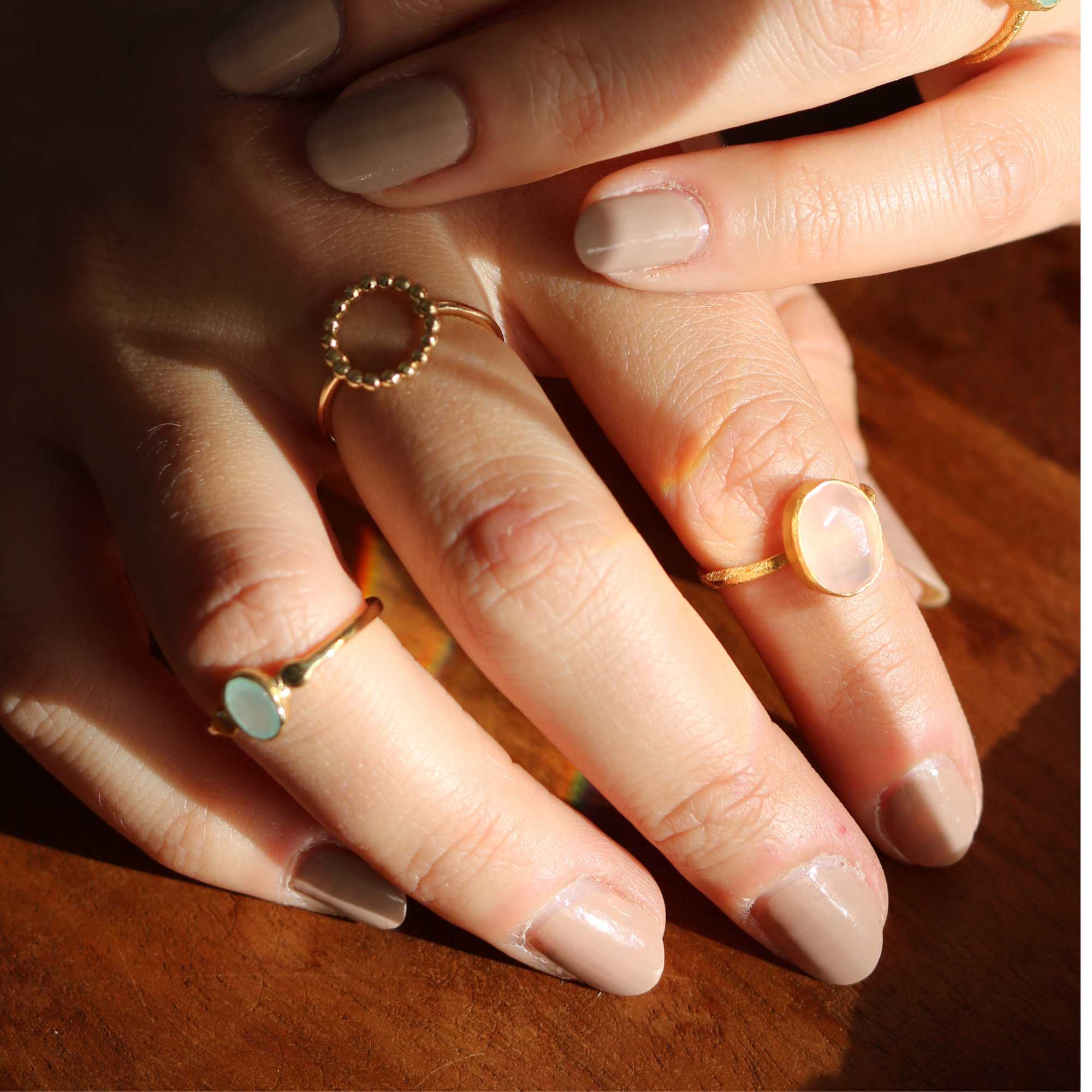 A gold adjustable ring featuring a small, bezel-set oval aqua chalcedony gemstone at its center, flanked by delicate metallic droplet accents on a smooth gold band.