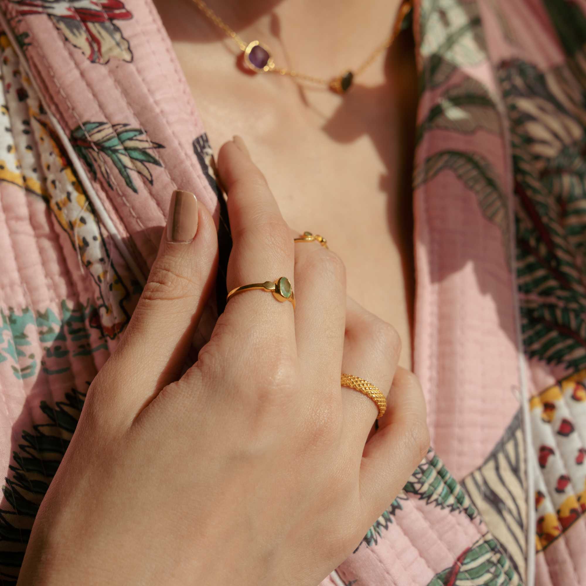 A gold adjustable ring featuring a small, bezel-set oval aqua chalcedony gemstone at its center, flanked by delicate metallic droplet accents on a smooth gold band.