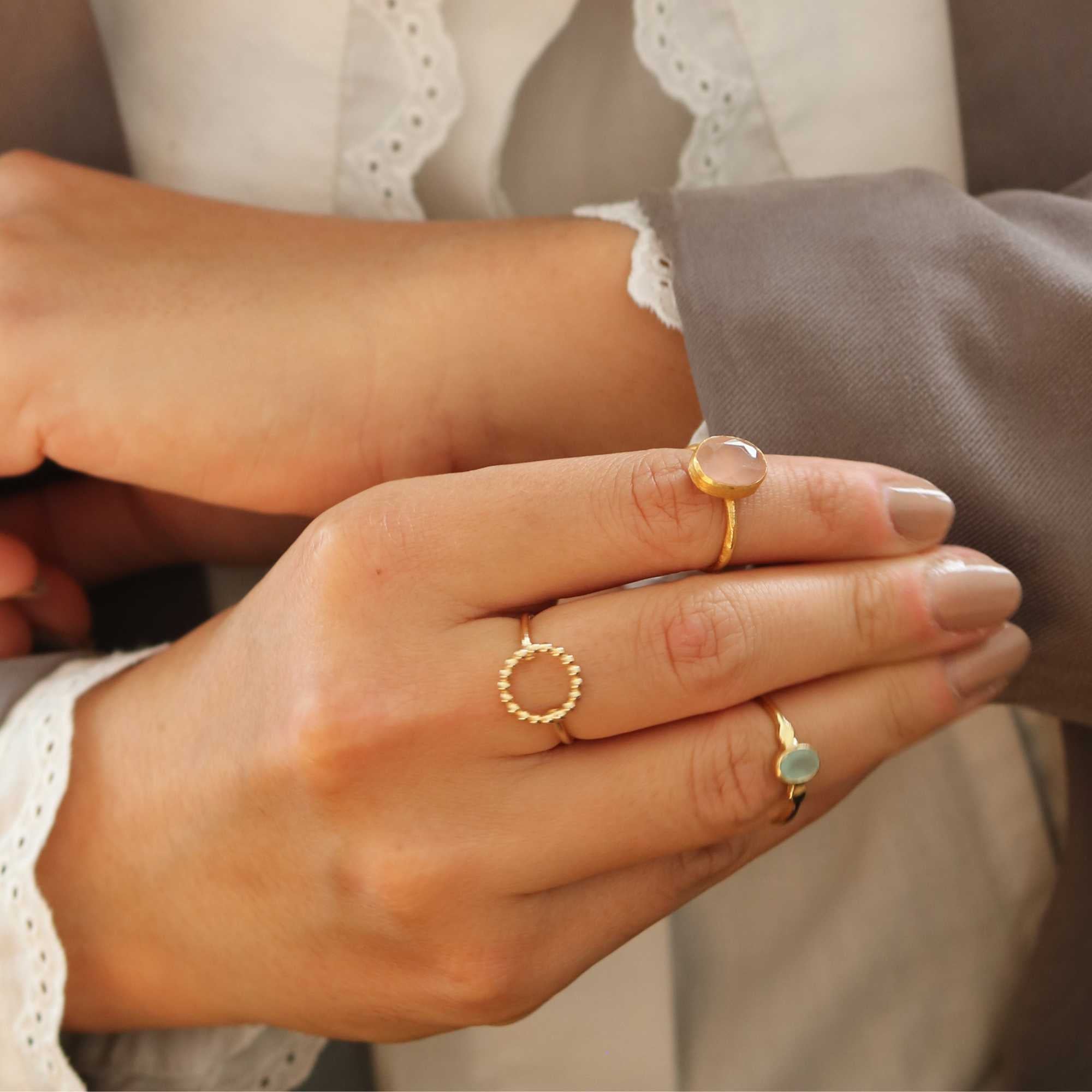 A gold adjustable ring featuring a small, bezel-set oval aqua chalcedony gemstone at its center, flanked by delicate metallic droplet accents on a smooth gold band.