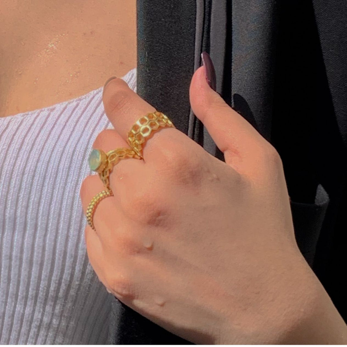 Gold honeycomb rings stacked with an aqua chalcedony ring and a beaded stacking ring on a model’s hand