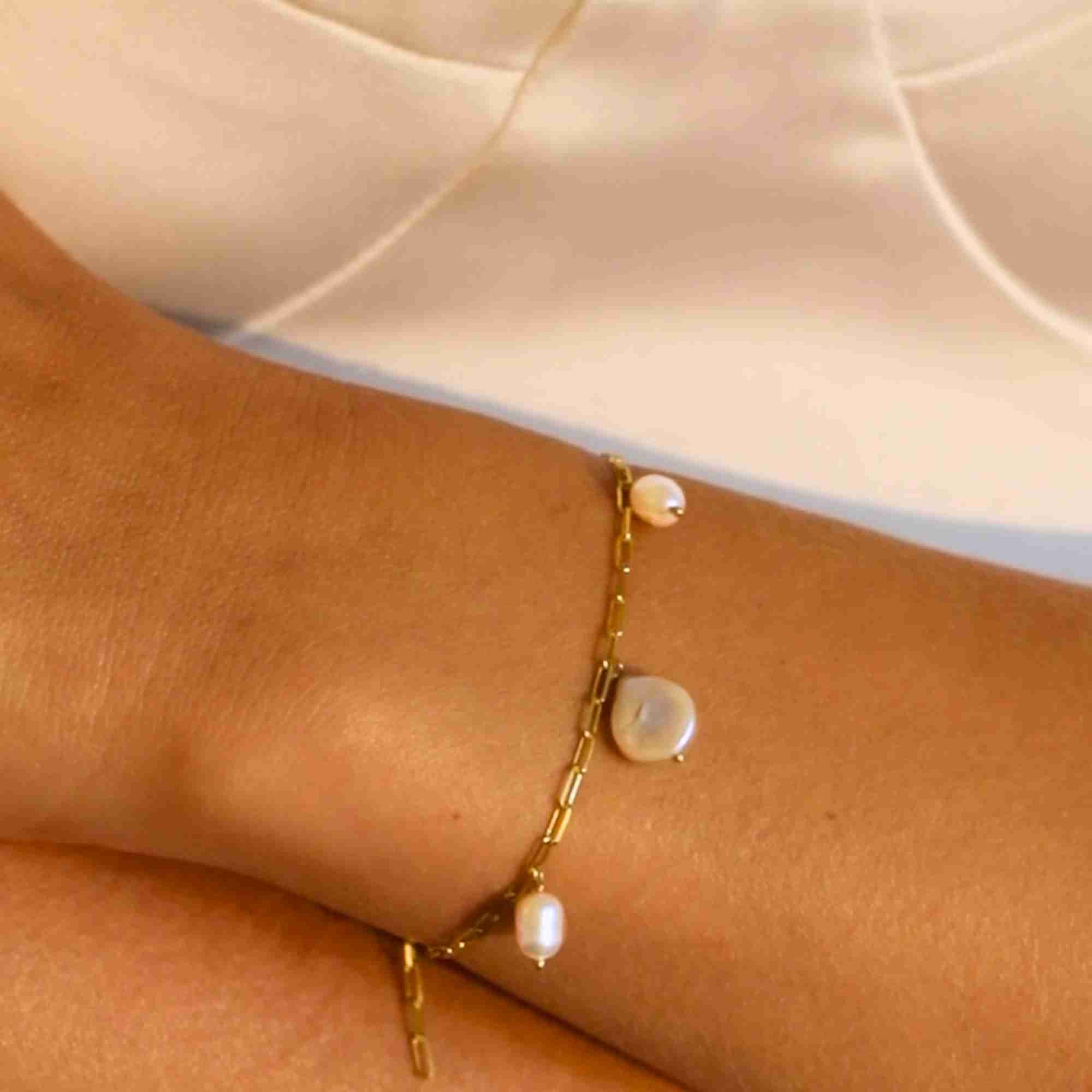 Macro close-up shot of a model's wrist showcasing the gold paperclip chain bracelet featuring three organic baroque pearl charms dangling along the link chain.