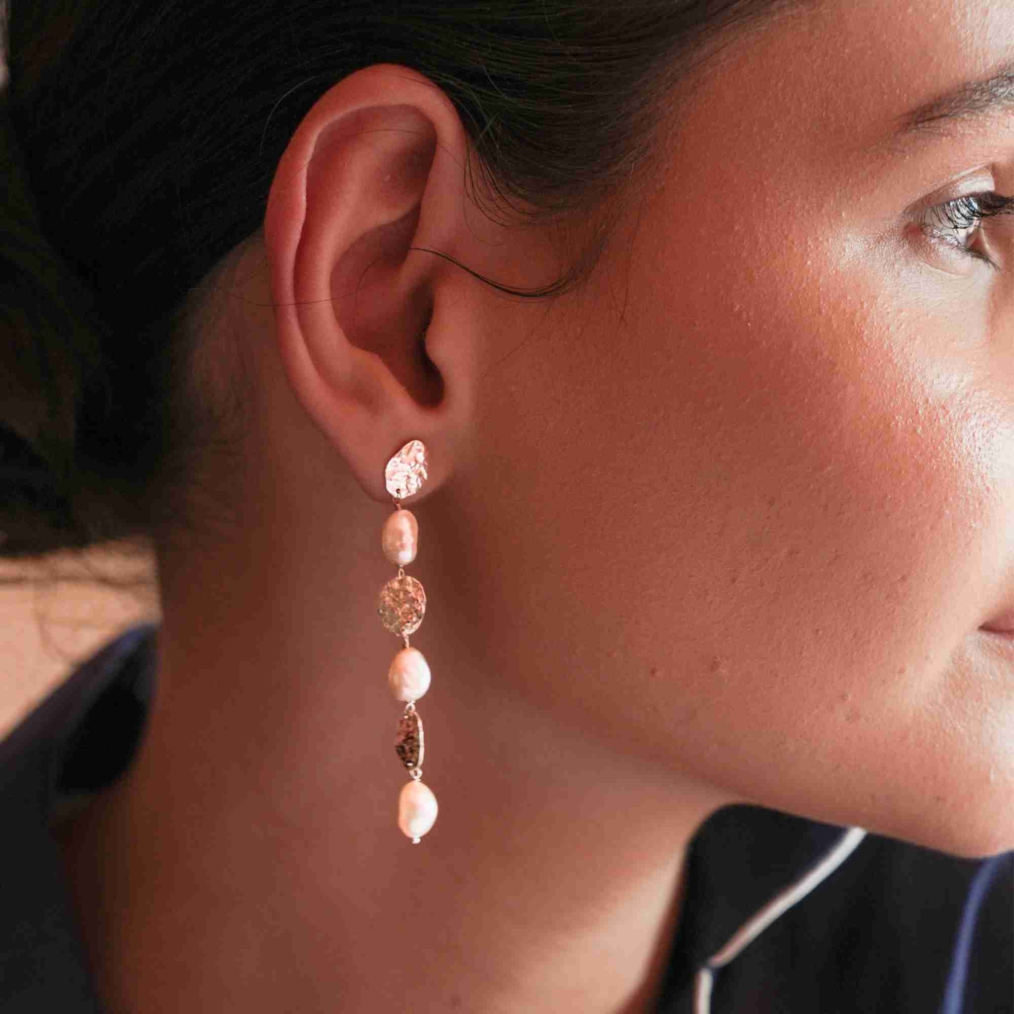 Side profile shot of a dark-haired model wearing the long gold molten disc and cascading pearl statement drop earring.