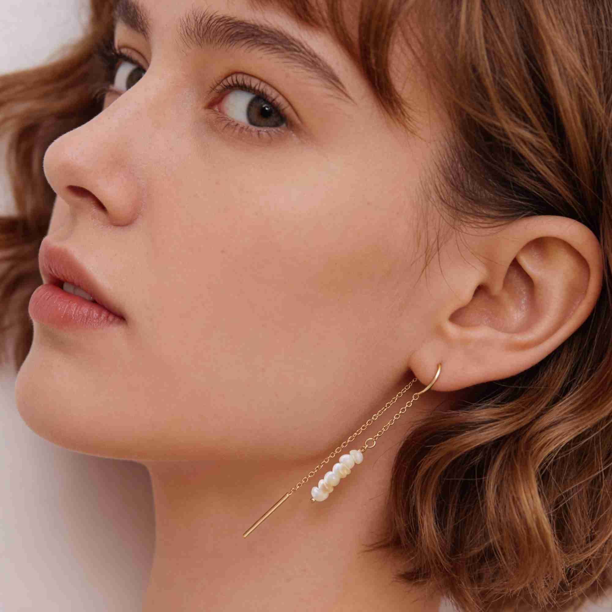 Three-quarter profile shot of a wavy-haired model showcasing the drape and detail of the gold seed pearl threader earring.