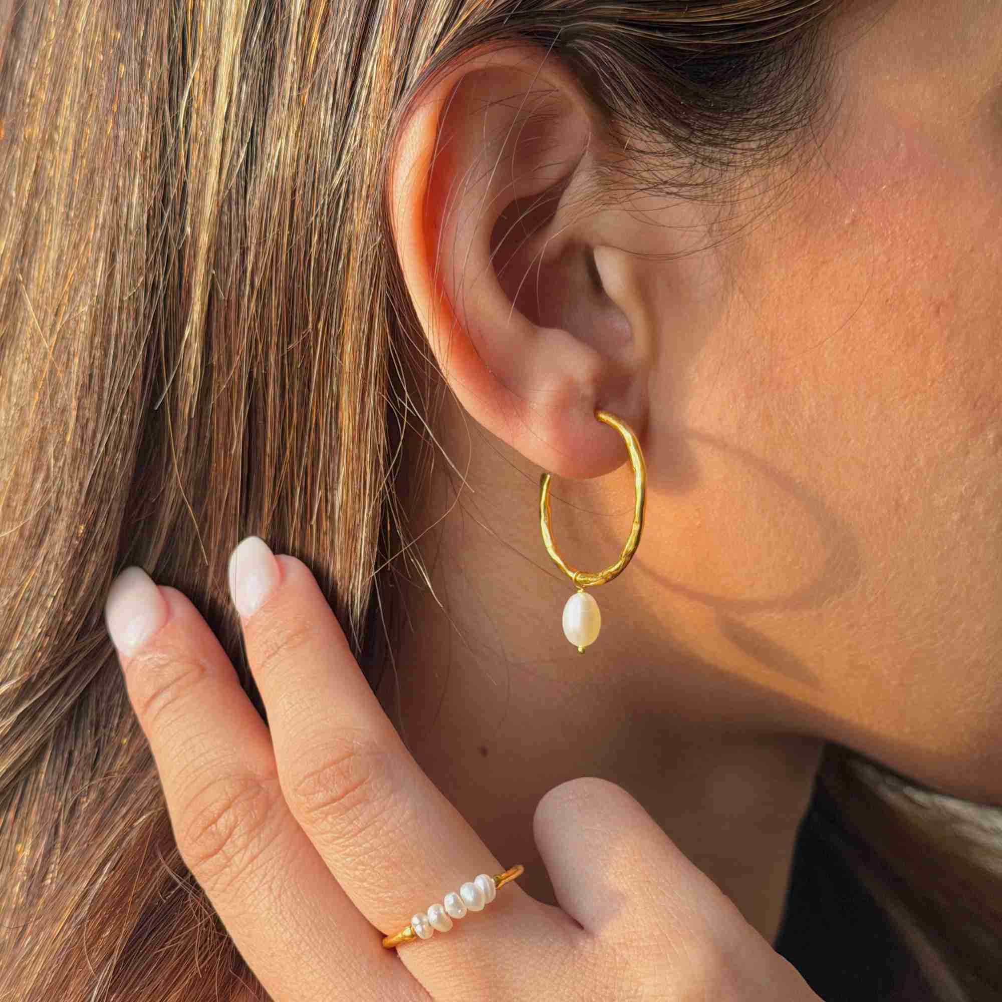  Side profile shot of a blonde model with her hand near her hair, displaying the gold teardrop pearl hoop earring and a matching gold pearl ring.