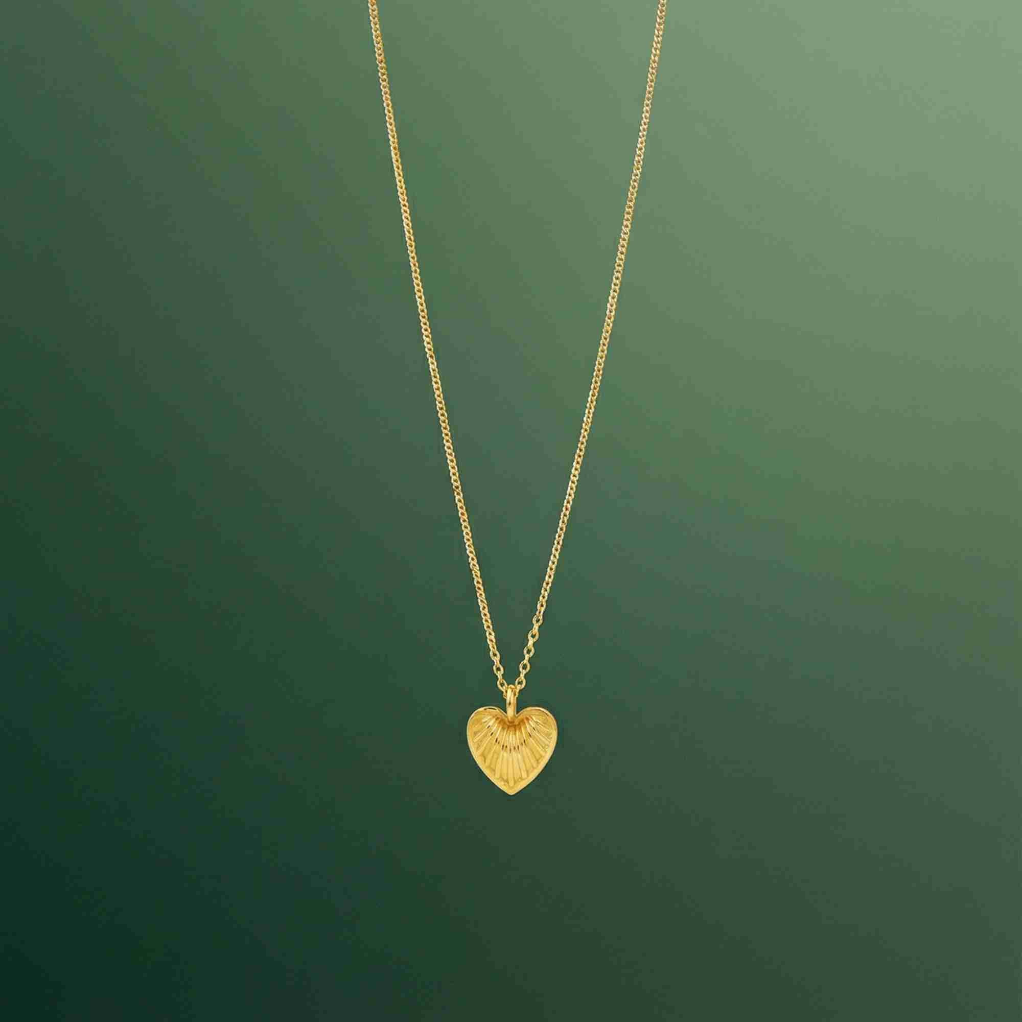 Gold Queen of Charms Fluted Heart Pendant Necklace featuring a ribbed, shell-like heart charm hanging from a delicate fine chain, displayed against a soft green gradient background.