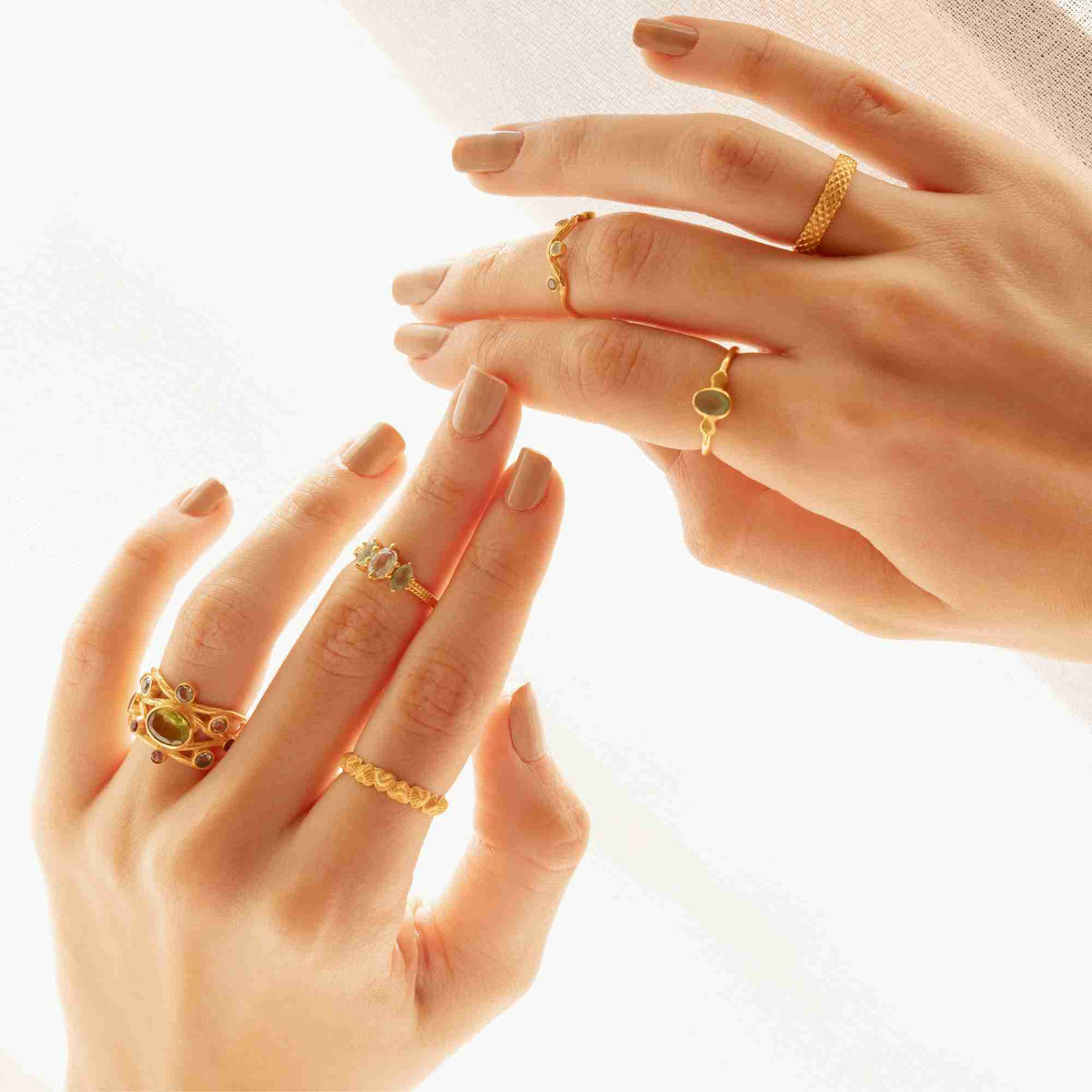 Brightly lit editorial shot of a model displaying both hands styled with multiple gold rings, featuring the fluted hearts eternity band on the index finger.