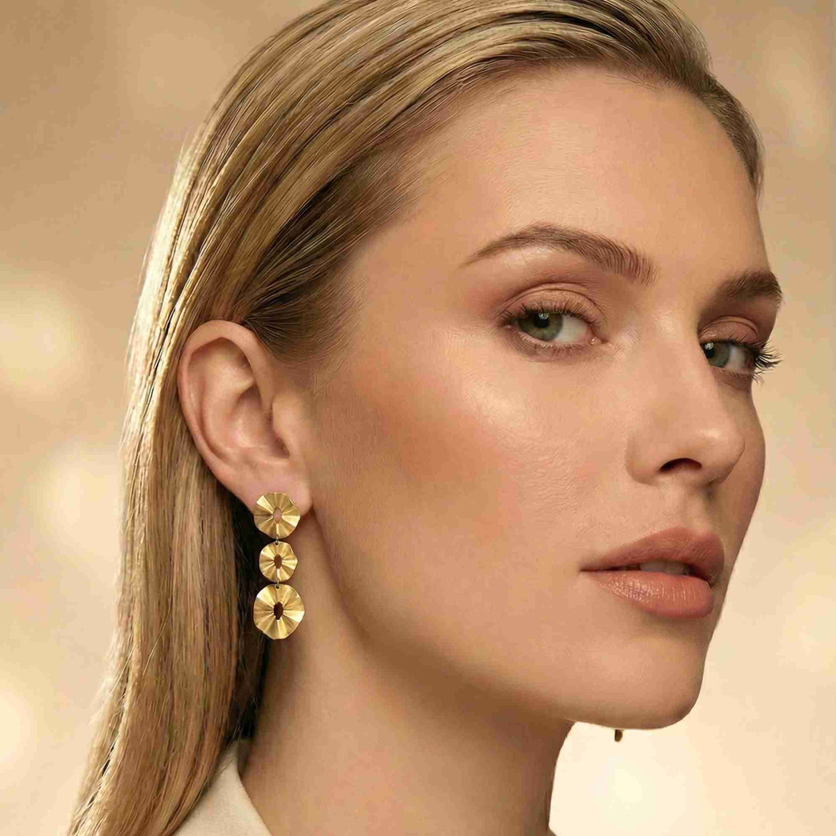 Studio portrait of a blonde model with slicked-back hair wearing gold cascading disc earrings
