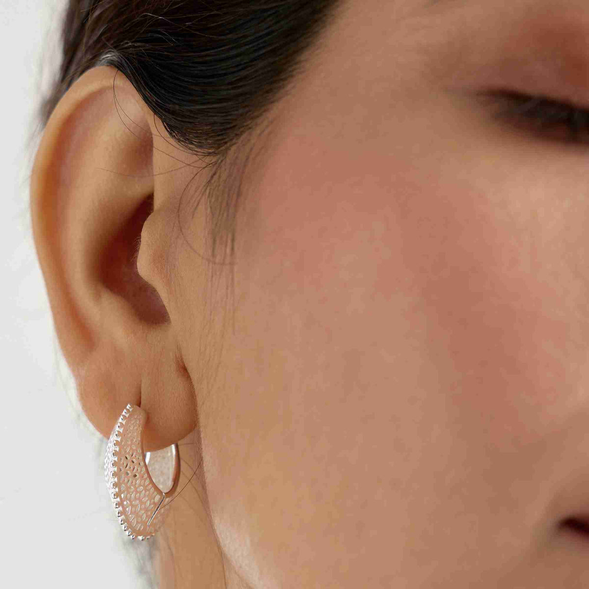 Extreme close-up shot of a model wearing the silver Ribbons & Lace Filigree Sculptural Hoop Earrings, displaying the tapered front profile and beaded edge details.