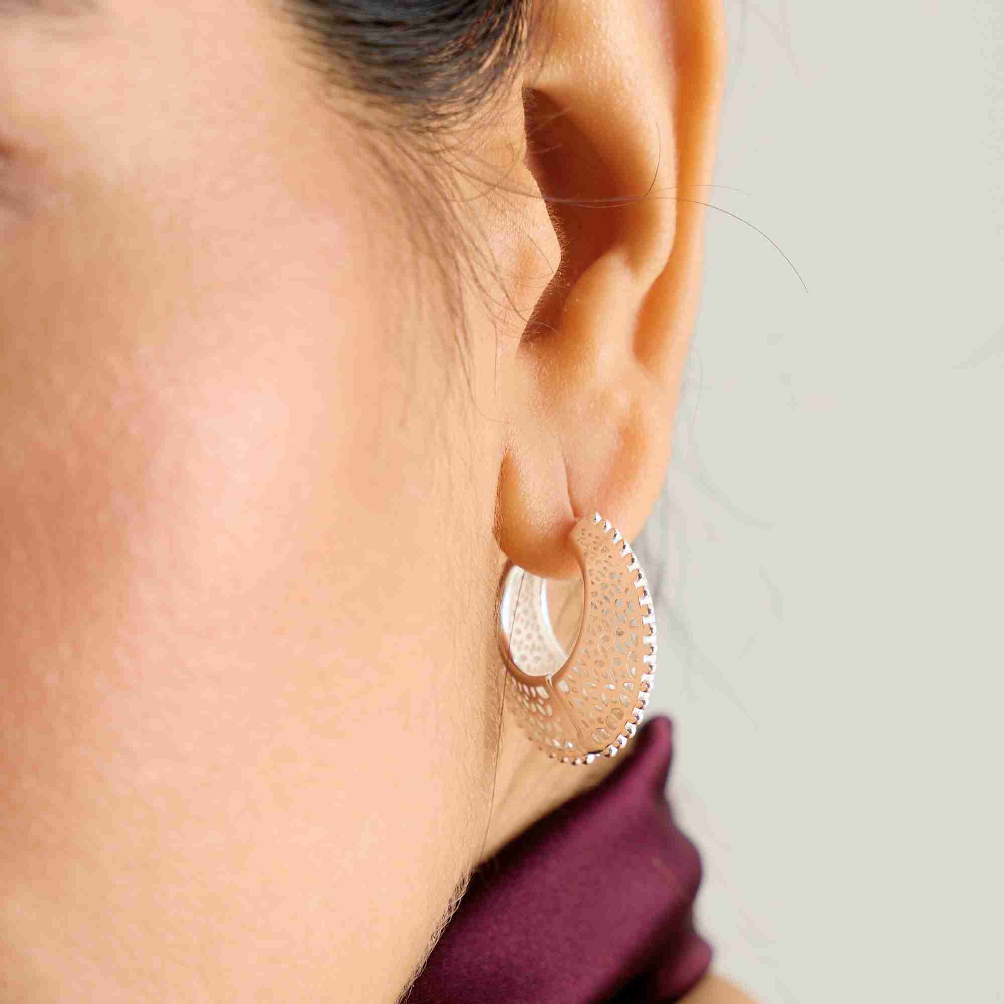 Close-up lifestyle view named Ribbon & Lace showing a model wearing the Ribbons & Lace Filigree Sculptural Hoop Earrings Silver, showcasing the wide, curved profile and intricate openwork lace pattern of the sterling silver hoop by Protsaah Zurich.