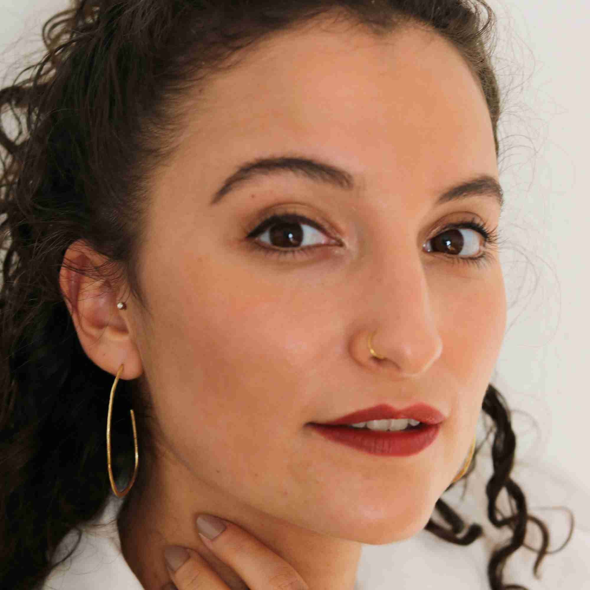 Studio portrait of a dark-haired model wearing the gold Ribbons & Lace Organic Oval Fine Hoop Earrings, facing slightly forward with bold red lipstick.