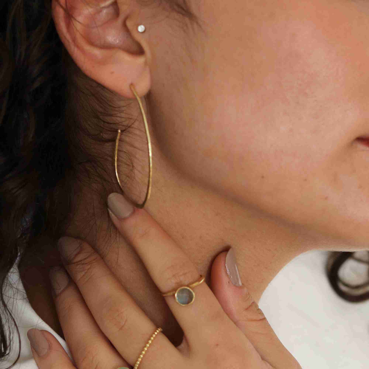 Close-up profile view of a model wearing the gold Ribbons & Lace Organic Oval Fine Hoop Earrings, touching her neck and showing the slender, organic curved shape of the hoop.