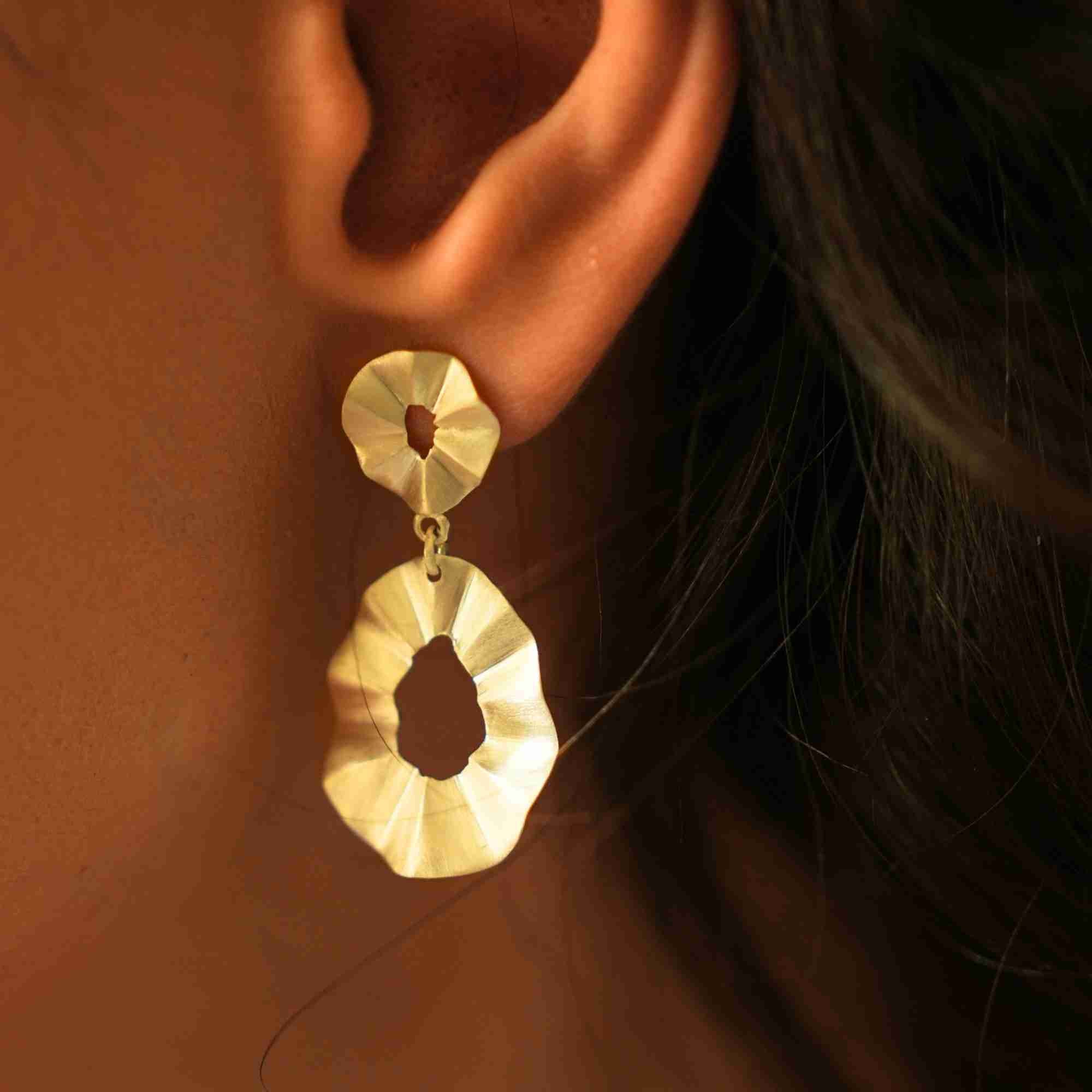 Extreme macro close-up of a model wearing the gold Ribbons & Lace Ruffle Fold Drop Statement Earrings, highlighting the textured, pleated double-ring ruffle design.