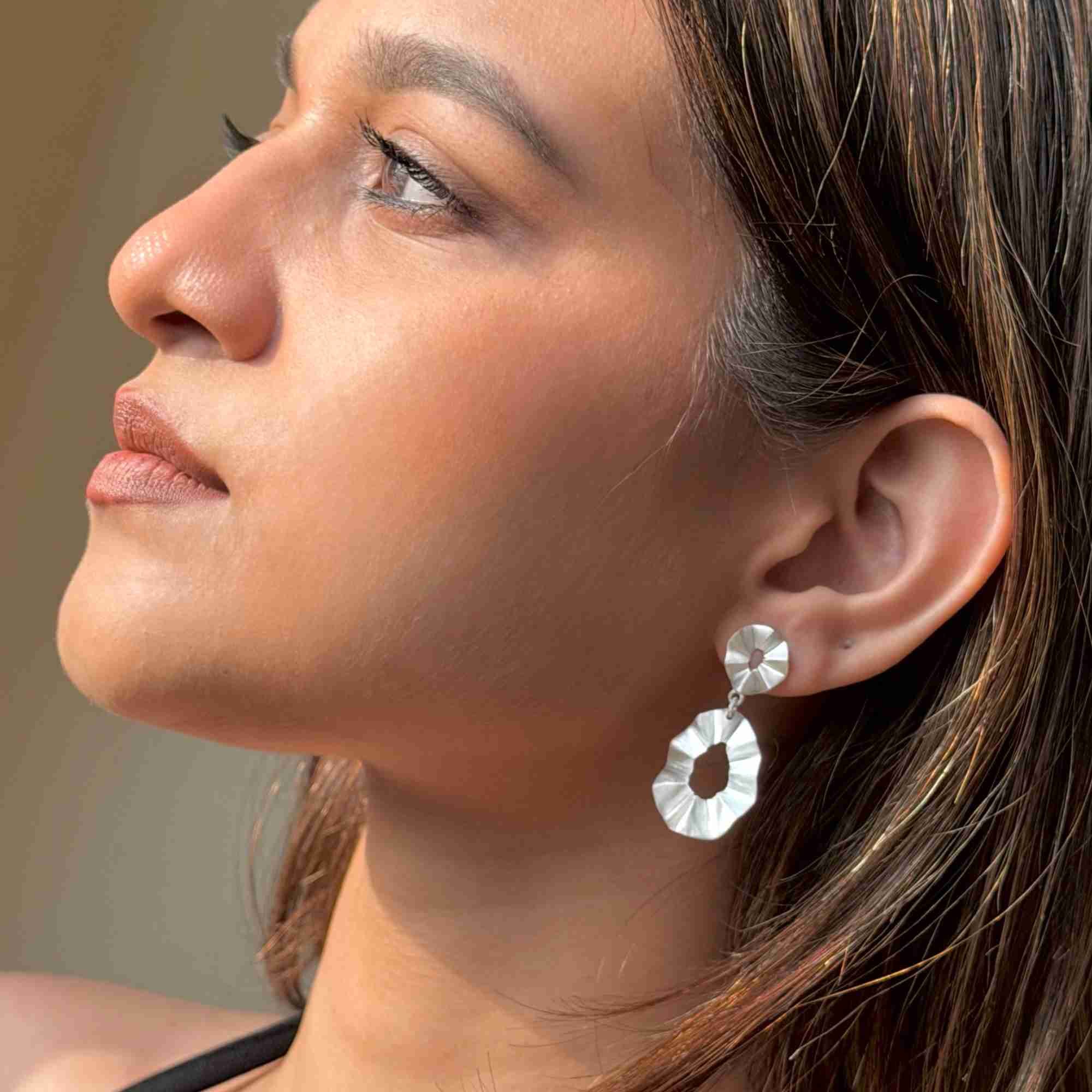 Low-angle side profile view of a model wearing the sterling silver Ribbons & Lace Ruffle Fold Drop Statement Earrings in natural light.