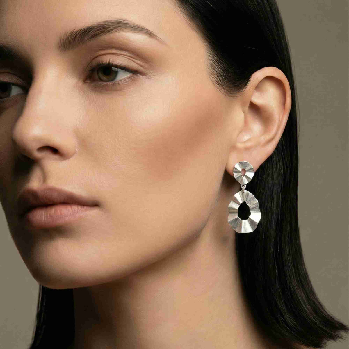 Studio portrait view of a model with sleek dark hair wearing the sterling silver Ribbons & Lace Ruffle Fold Drop Statement Earrings.