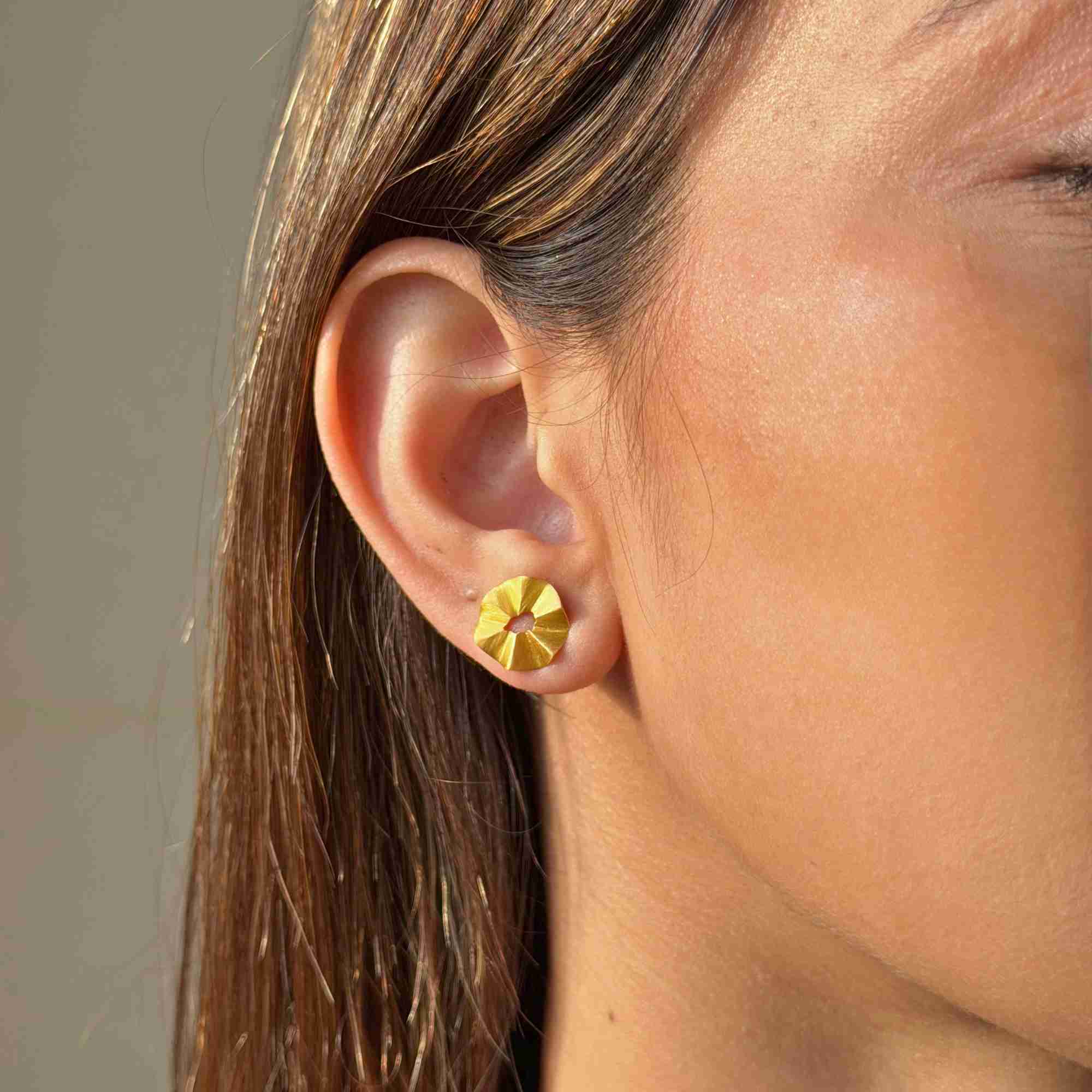Close-up profile view of a model's ear featuring the gold Ribbons & Lace Ruffle Fold Stud Earrings, highlighting the folded, pleated disc design.