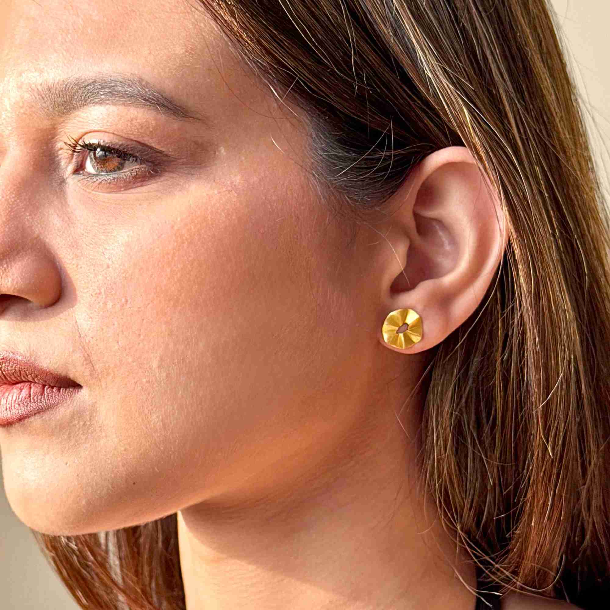 Three-quarter profile shot of a model wearing the gold Ribbons & Lace Ruffle Fold Stud Earrings, showing the small textured flower-like ruffled disc shape on the lobe.