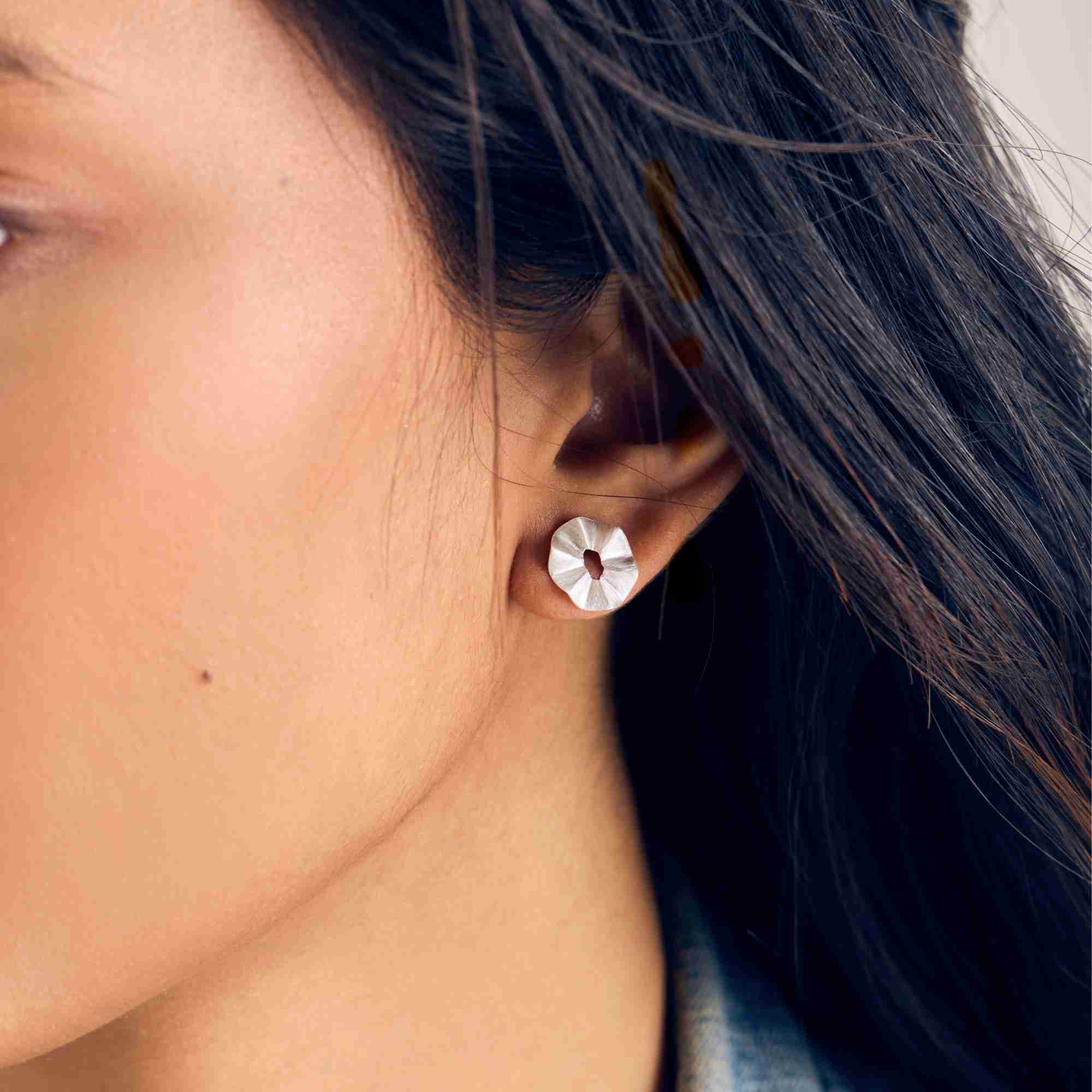 Close-up model view named Ribbon & Lace (2).jpg showing a woman wearing the Ribbons & Lace Ruffle Fold Stud Earrings Silver, showcasing the textured, hand-brushed matte silver finish shaped into a delicate, three-dimensional ruffled fold design by Protsaah Zurich.