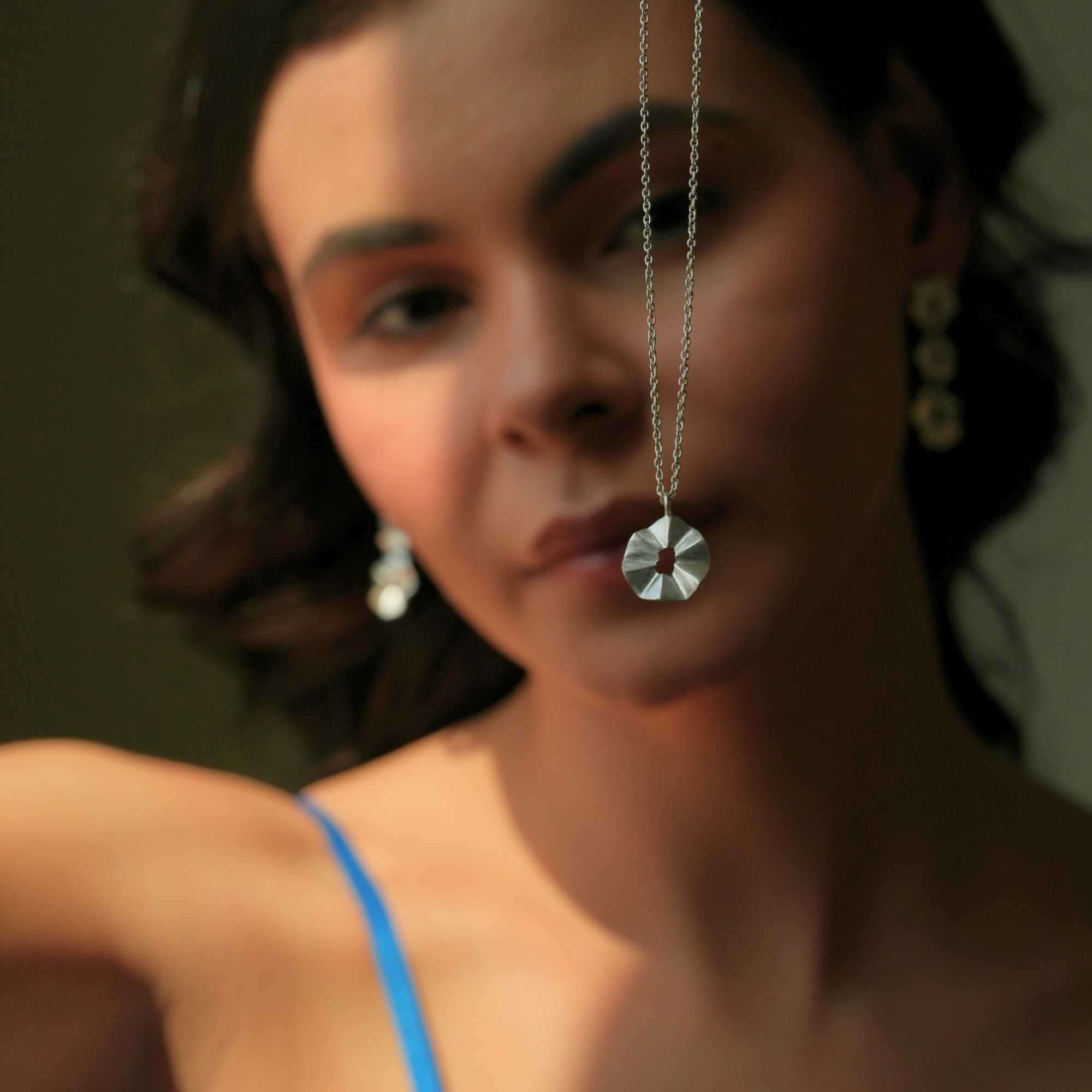 A model wearing the Ribbons & Lace Ruffle Furls Pendant Necklace in silver, showcasing a delicately textured, organic ruffled disc pendant suspended from a fine silver chain.