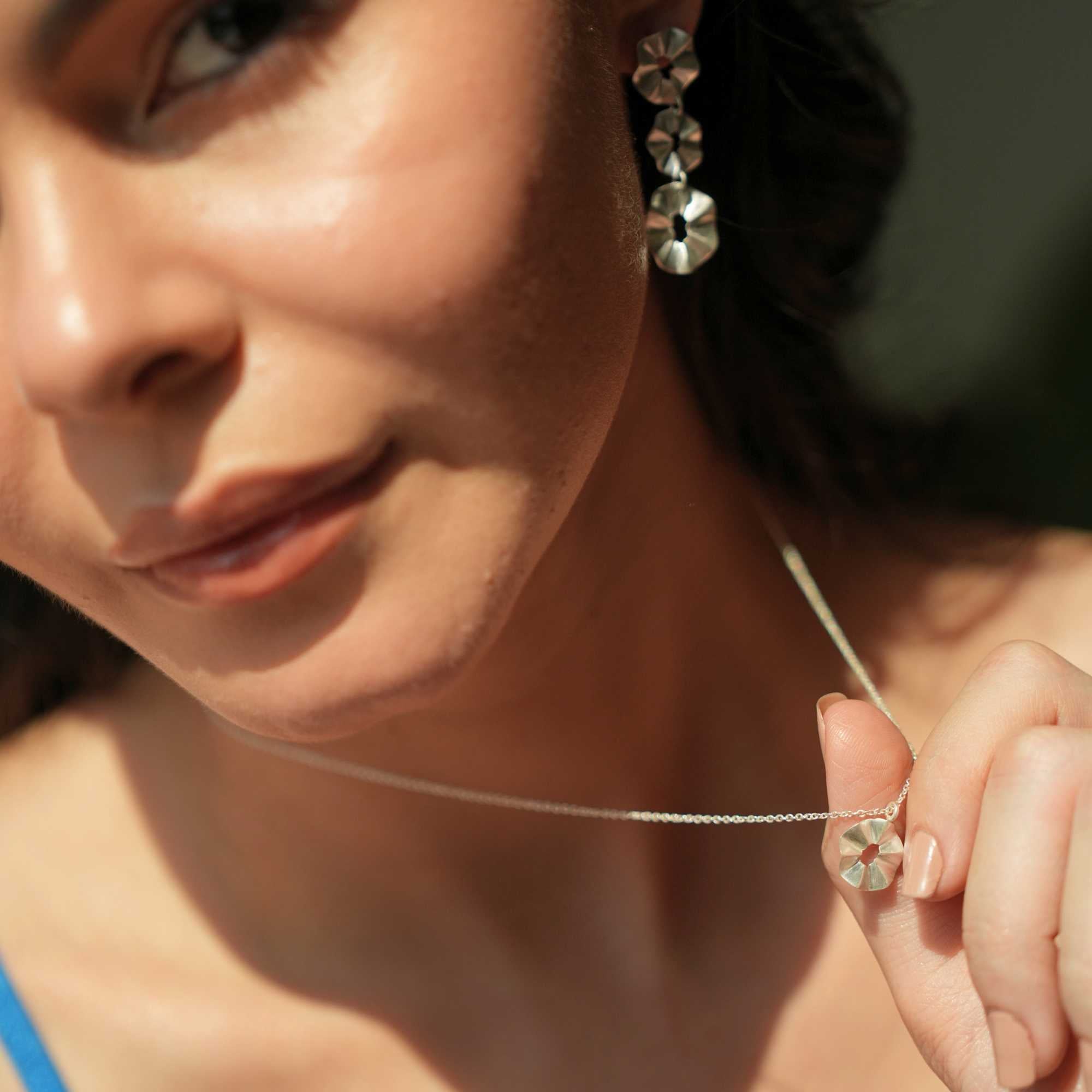 A model wearing the Ribbons & Lace Ruffle Furls Pendant Necklace in silver, showcasing a delicately textured, organic ruffled disc pendant suspended from a fine silver chain.