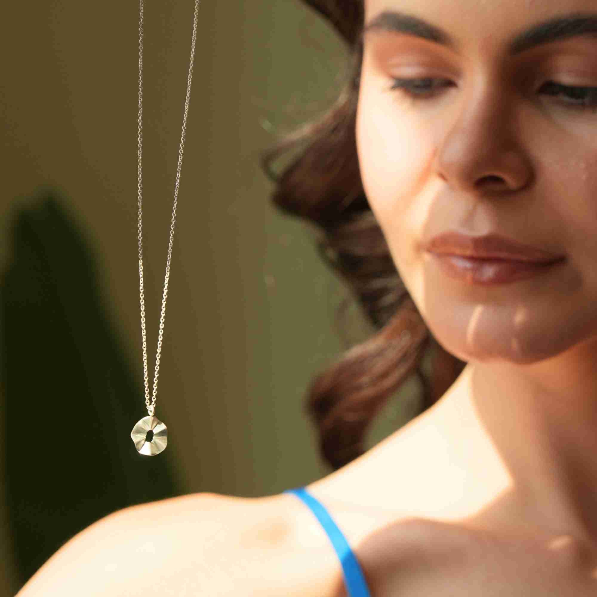 Warmly lit portrait shot featuring the silver Ribbons & Lace Ruffle Furls Pendant Necklace hanging over a model's shoulder in natural sunlight.