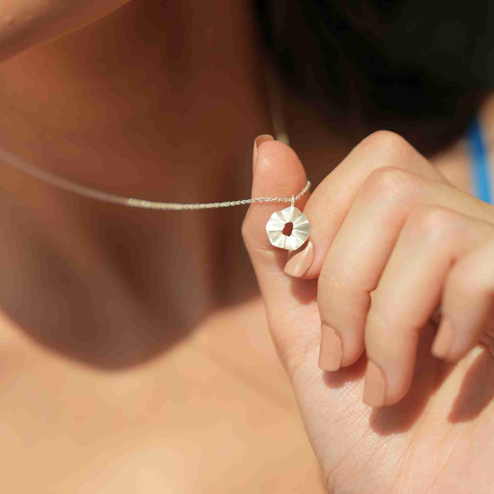 Macro close-up of a model holding the small, ruffled disc charm of the silver Ribbons & Lace Ruffle Furls Pendant Necklace between her fingers.