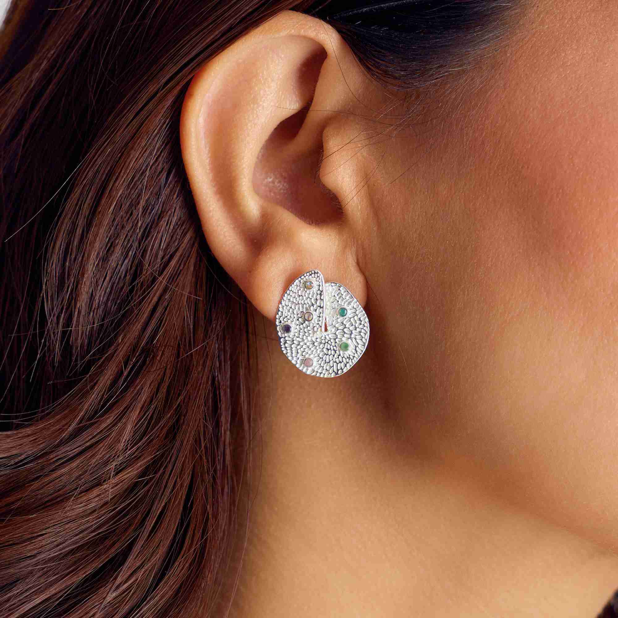 Close-up model view named Ribbon & Lace showing a woman wearing the Ribbons and Lace Galaxy Multi-Gemstone Stud Earrings Silver, showcasing the large, organically shaped sterling silver disc with an intricate textured lace pattern studded with tiny, multi-colored embedded gemstones by Protsaah Zurich.