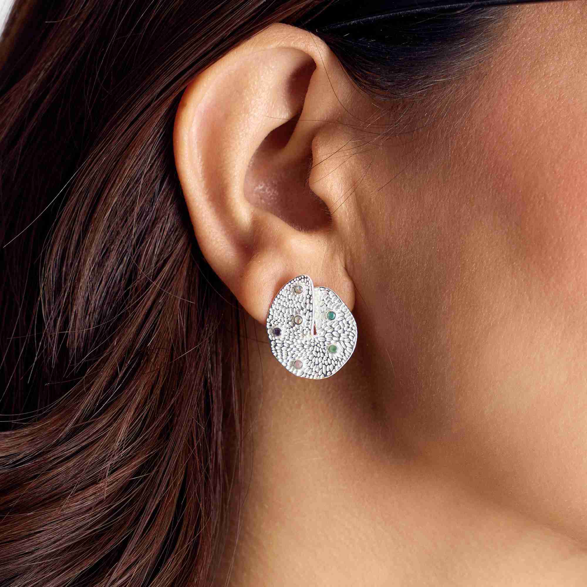 Extreme close-up shot of the ear featuring the textured silver Ribbons and Lace Galaxy Multi-Gemstone Stud Earrings with embedded multi-colored gemstones.