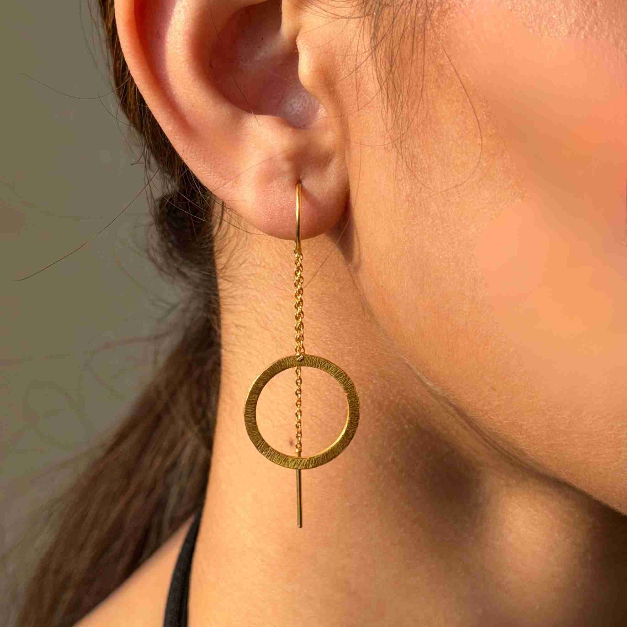 Close-up shot of a model's ear wearing the gold Shimmering Disks Circle Chain Threader Earring, showcasing the hand-brushed circular disc and delicate chain extension.