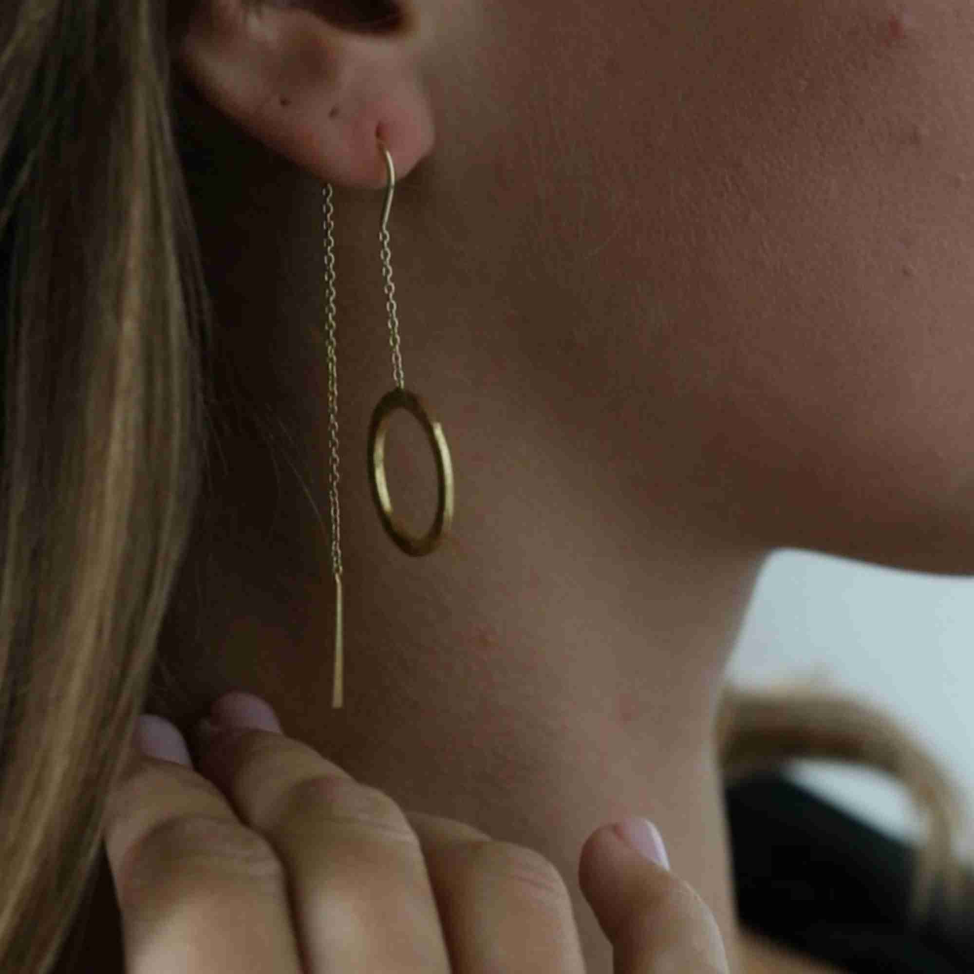 Soft close-up view of a model wearing the gold circle threader earring, highlighting how the chain dangles alongside the neck.