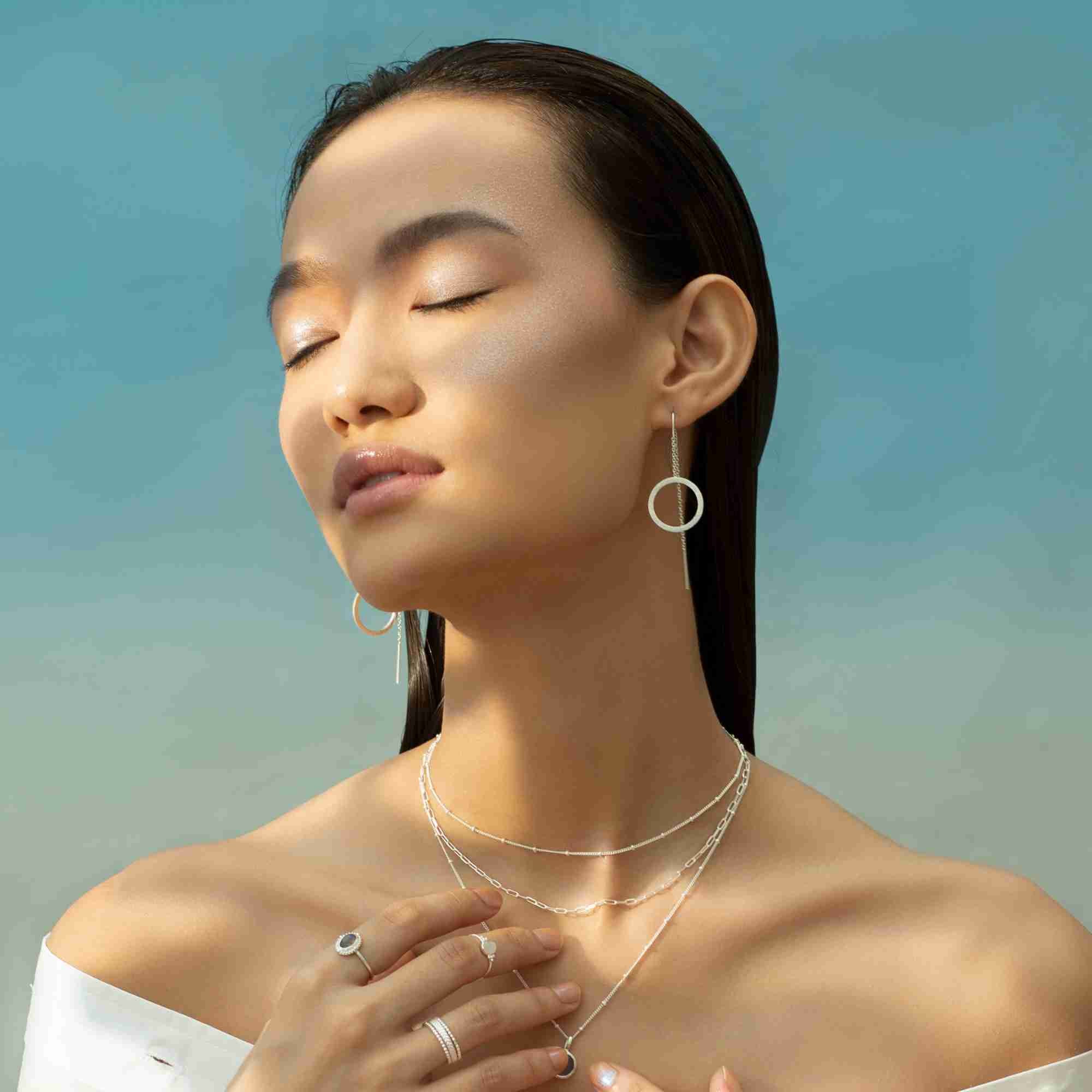 Model styled with the silver Shimmering Disks Circle Chain Threader Earring paired with layered silver necklaces under soft natural light.
