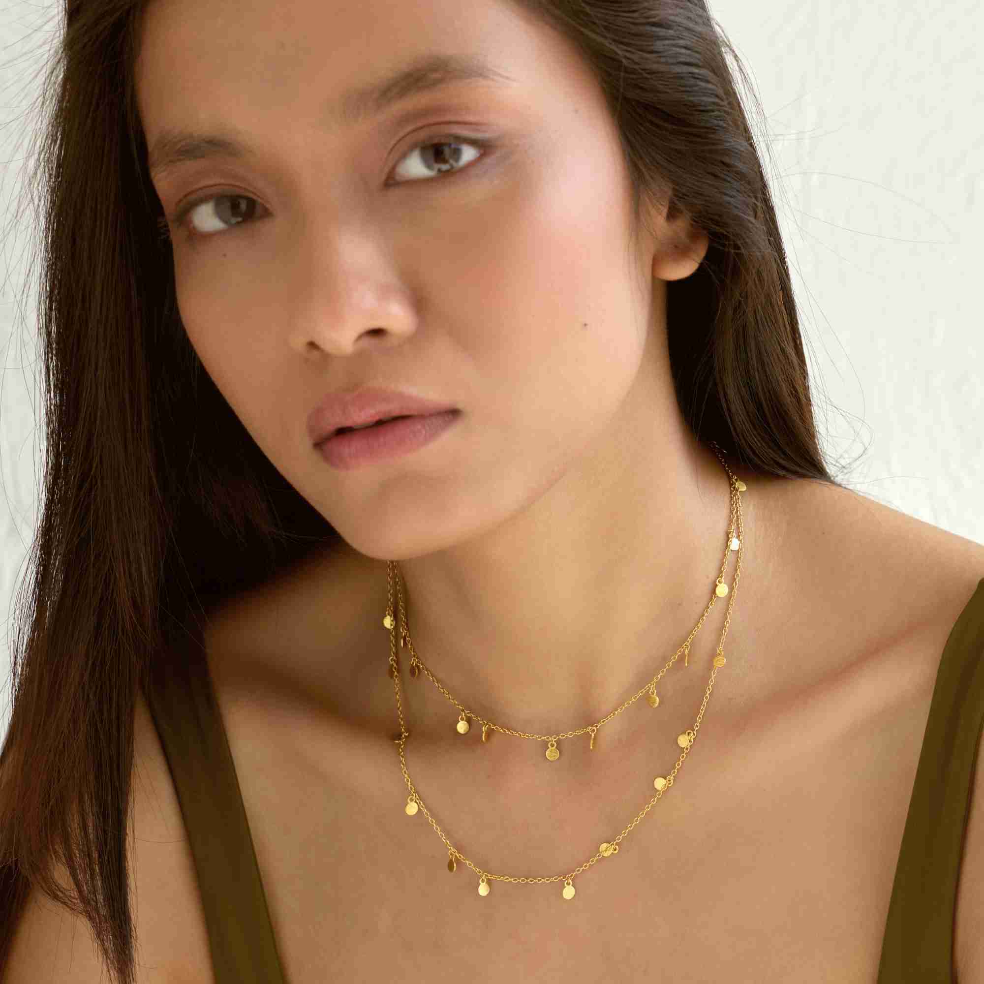Model wearing the long gold Shimmering Disks Constellation Disc Chain Necklace wrapped twice around her neck as a layered choker and short necklace.