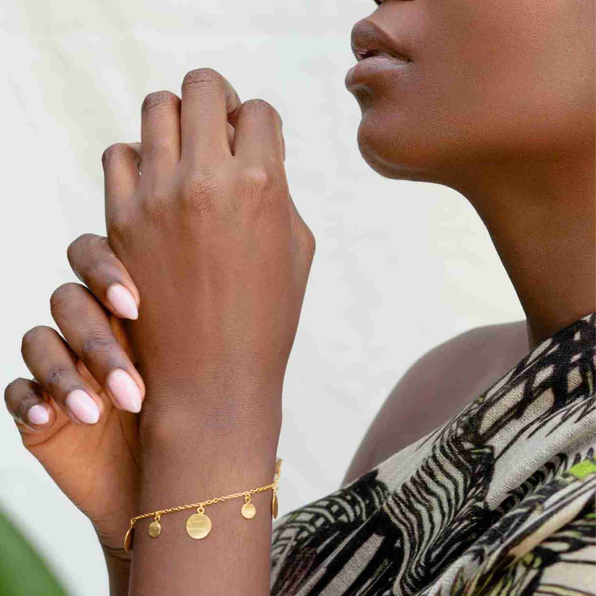 Model with clasped hands wearing the gold Shimmering Disks Delicate Chain Bracelet, highlighting the dangling textured disc charms.