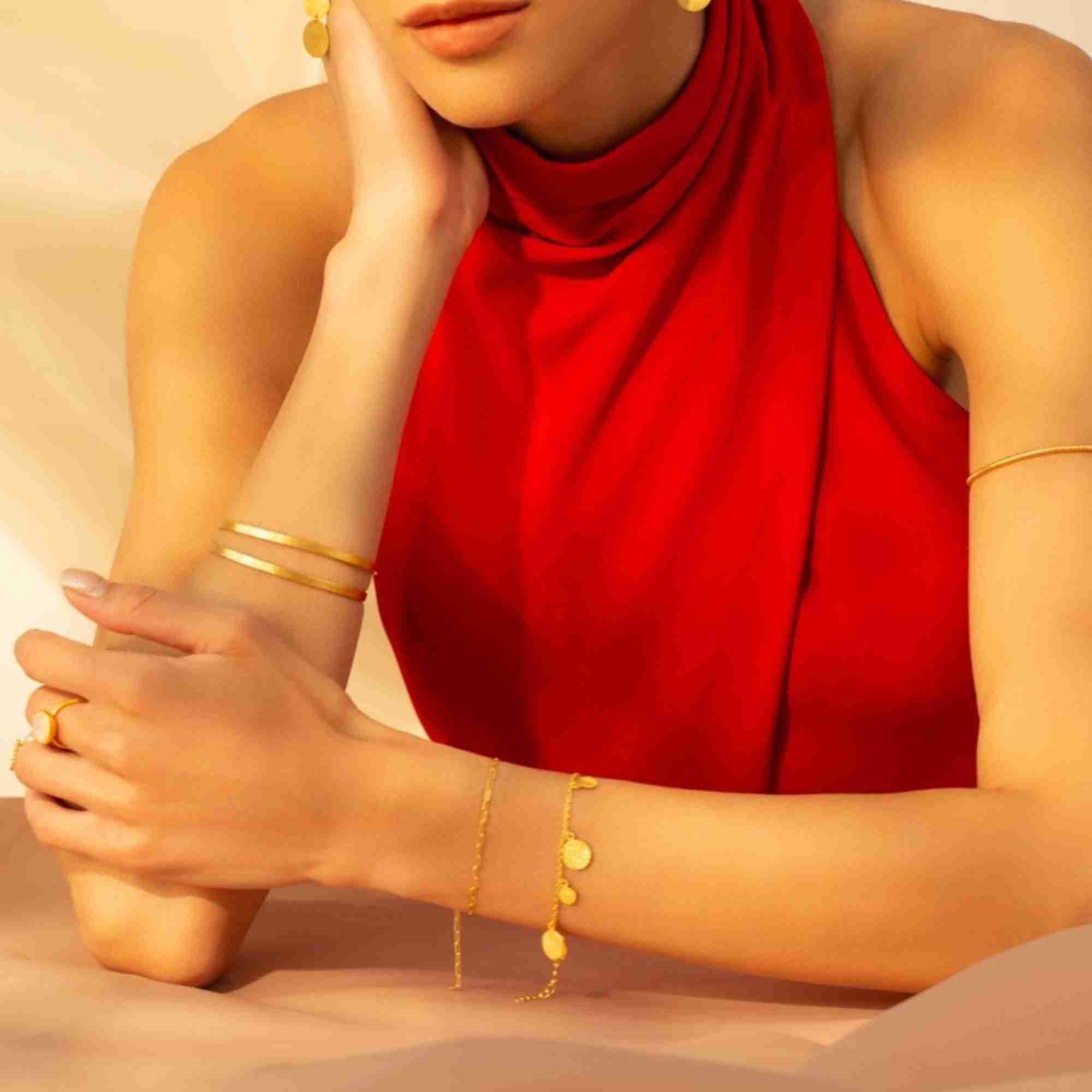 tudio product shot of the Shimmering Disks Delicate Chain Bracelet Gold laid out flat on a textured white surface, showcasing the entire dainty silhouette and geometric disc design.