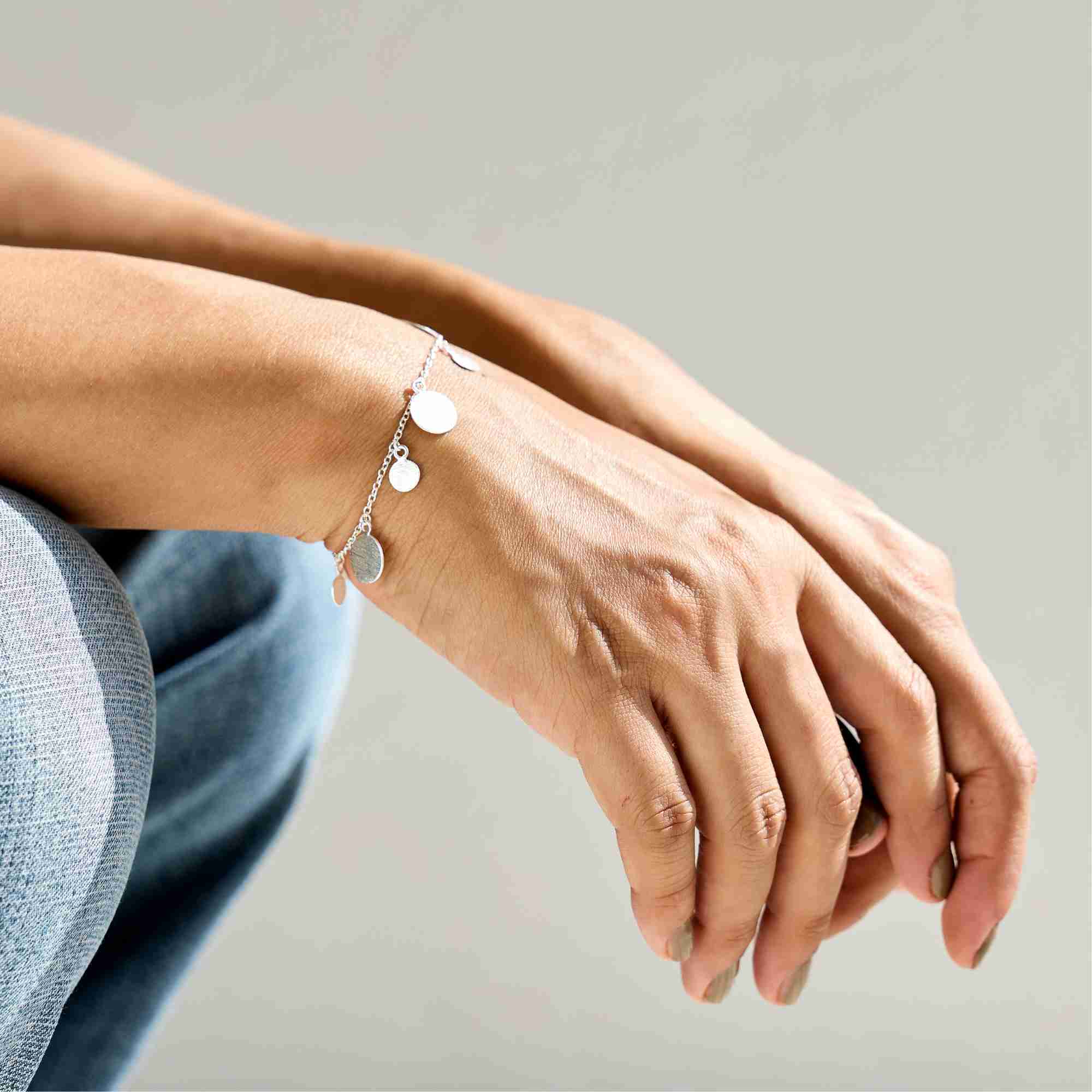 Close-up shot of a model resting her hands while wearing the silver Shimmering Disks Delicate Chain Bracelet featuring small dangling brushed disc charms.