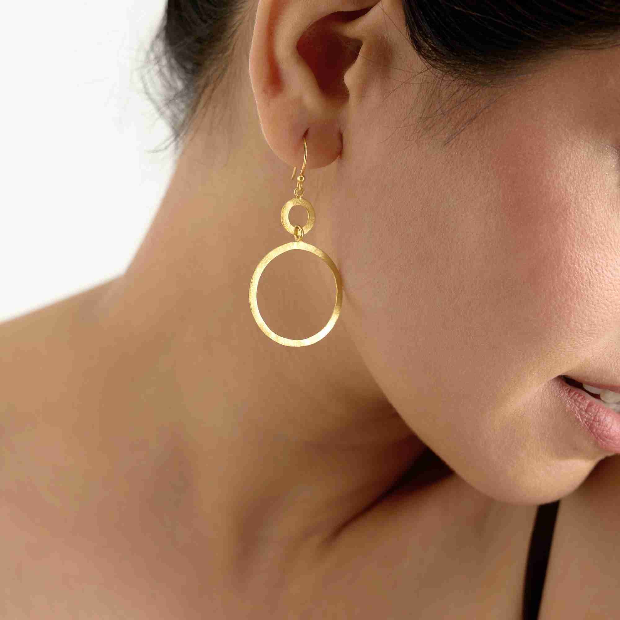 Side view of a model wearing the gold Shimmering Disks Dual Circle Statement Earring, showcasing the double drop open-circle silhouette.