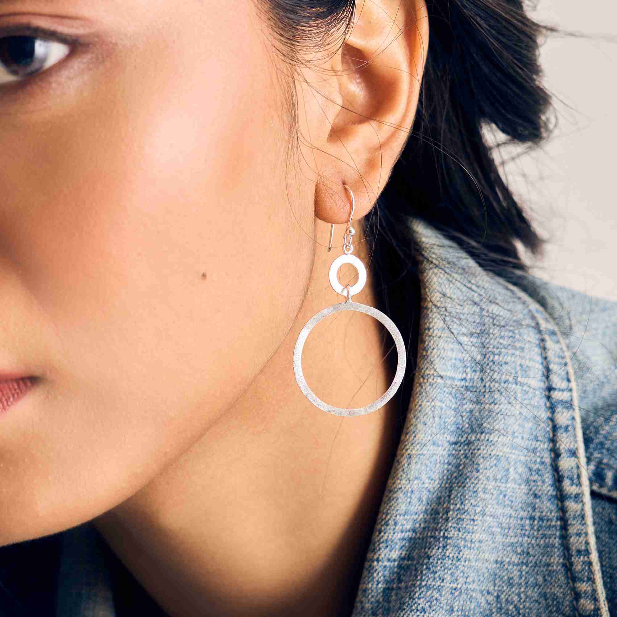 Profile side view of a model wearing Shimmering Disks Dual Circle Statement Earrings Silver, highlighting the sculptural form and clean geometric silhouette of the overlapping matte circles from the side angle.