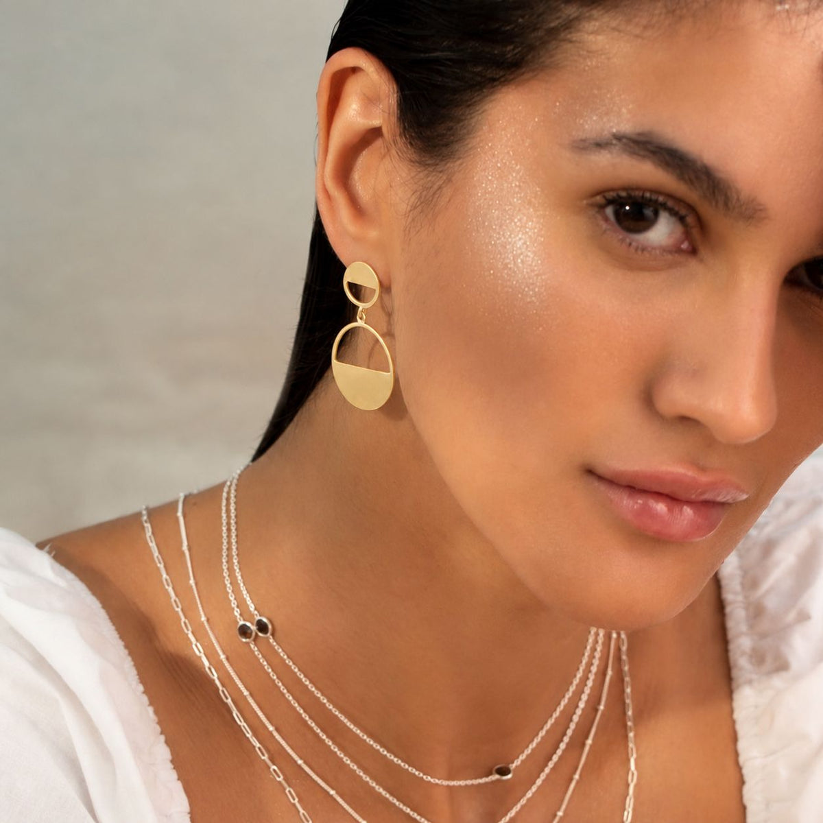 Model with sleek dark hair wearing a Horizon Half-Moon Drop earring in Gold, with layered silver chains