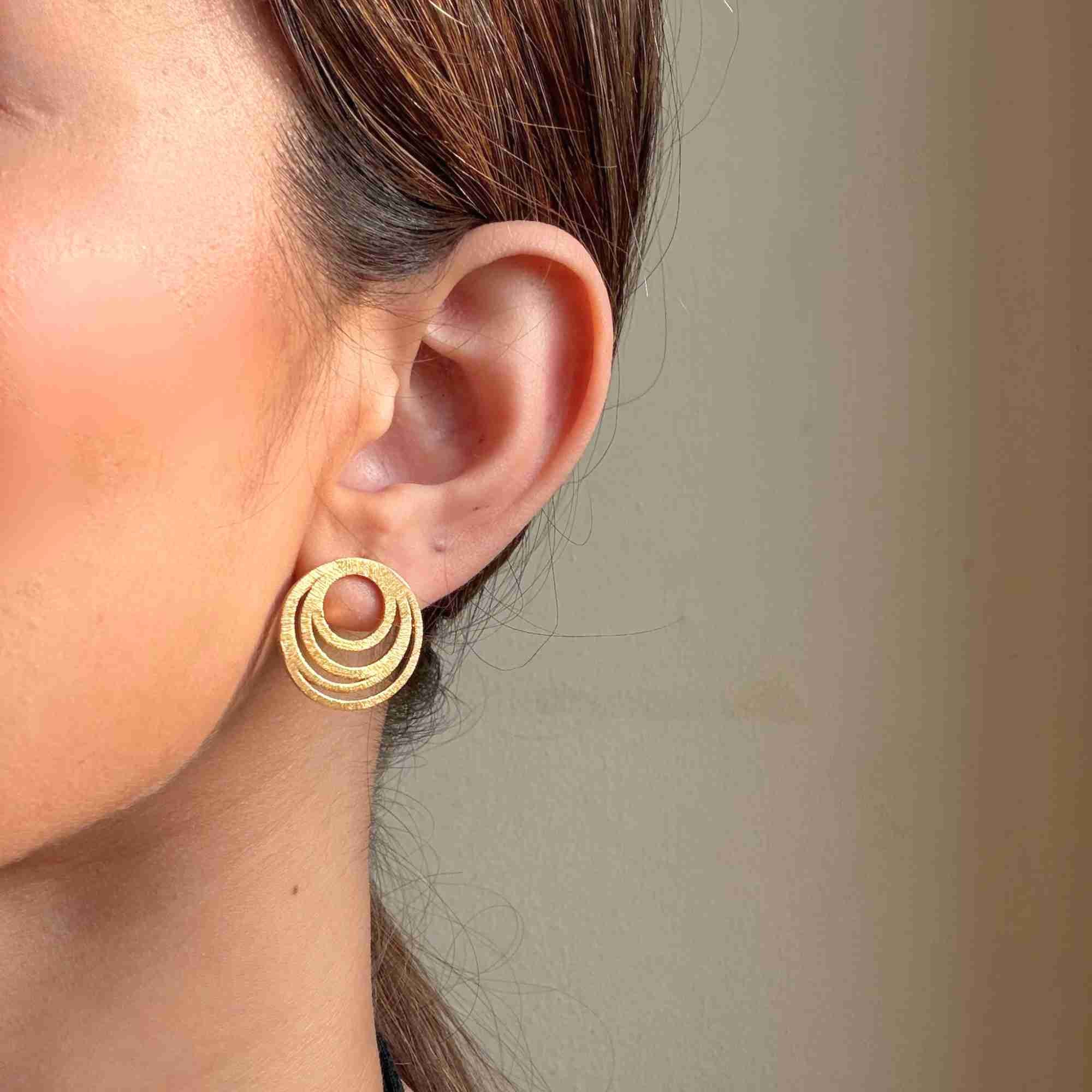 Close-up profile view of a model wearing the gold Shimmering Disks Intermingled Circles Stud Earrings, highlighting the textured finish on three concentric, interlocking rings.