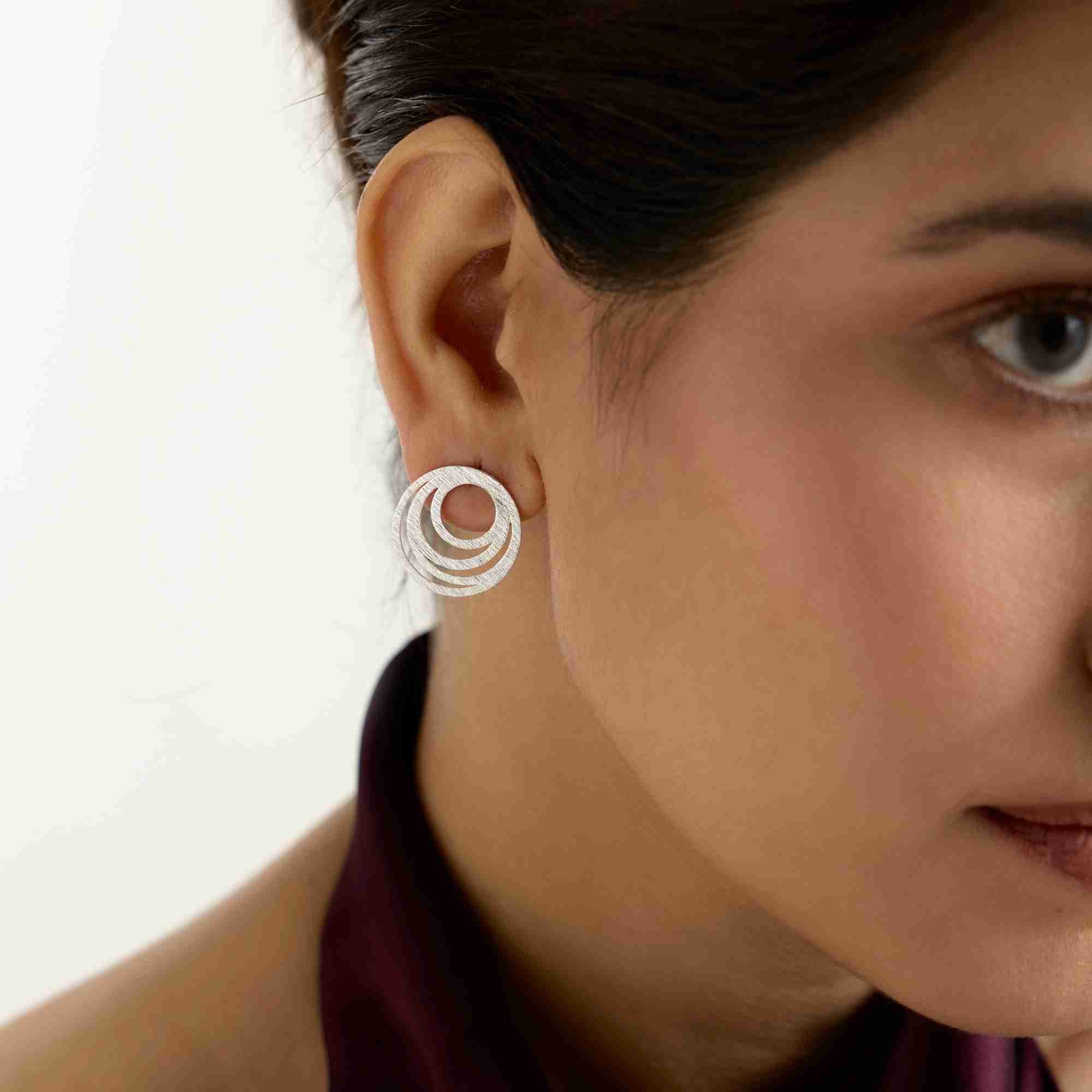 Model wearing the Shimmering Disks Intermingled Circles Stud Earrings in silver, featuring nested concentric open circles with a brushed finish.