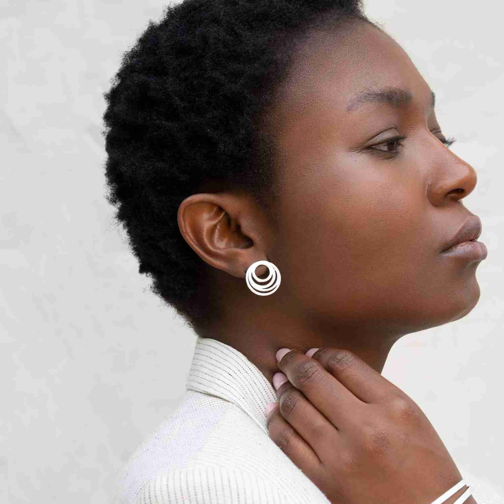 Profile view of a model styled with the silver Shimmering Disks Intermingled Circles Stud Earrings, showcasing the layered circular geometric design.