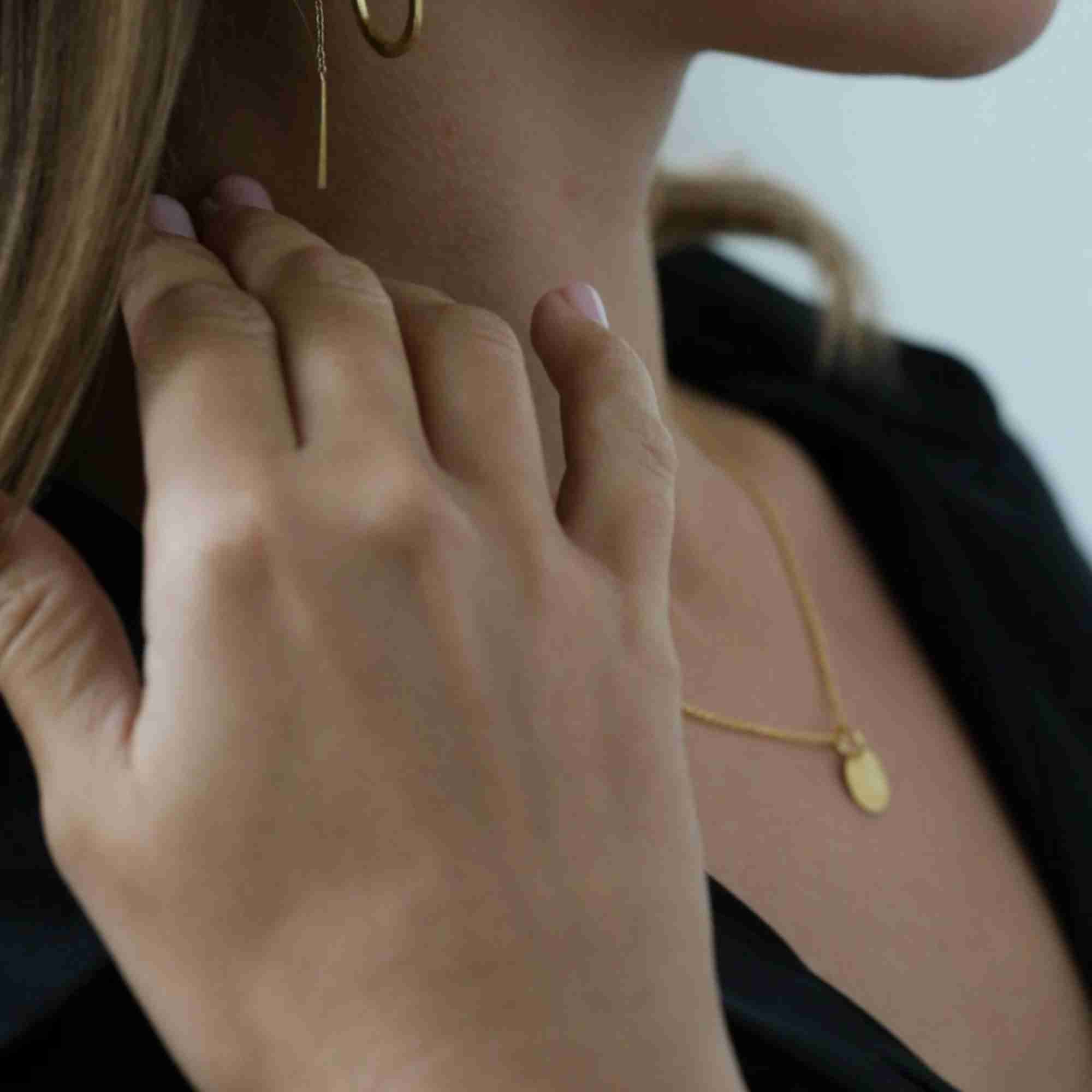 Side profile model view named Shimmering Disks (59)_2.jpg showing a woman wearing the Shimmering Disks Minimalist Coin Pendant Necklace Gold with a dark black top, highlighting the delicate gold link chain and small circular pendant resting elegantly on her chest by Protsaah Zurich.