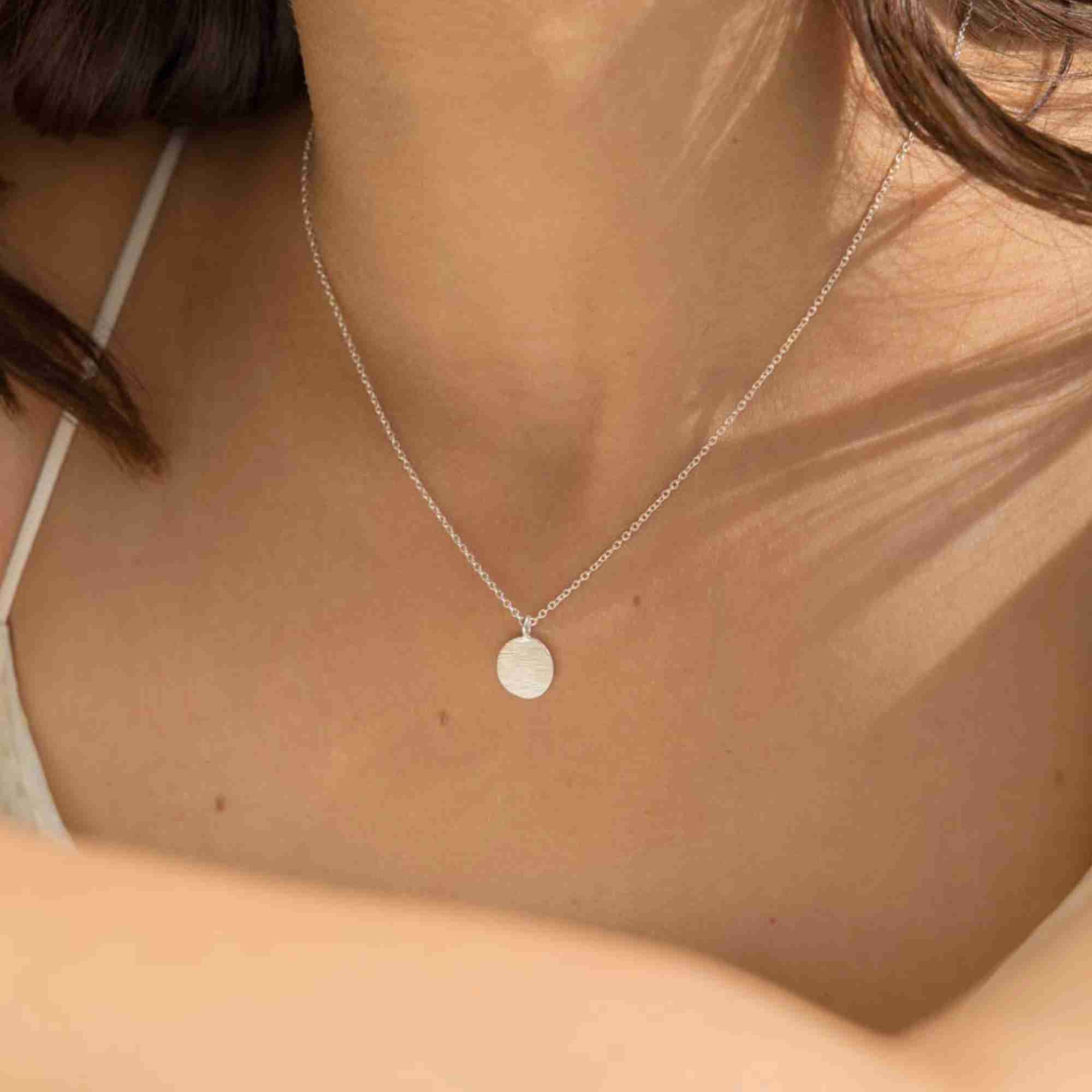Front-facing close-up showing the silver Shimmering Disks Minimalist Coin Pendant Necklace paired with a white top strap.