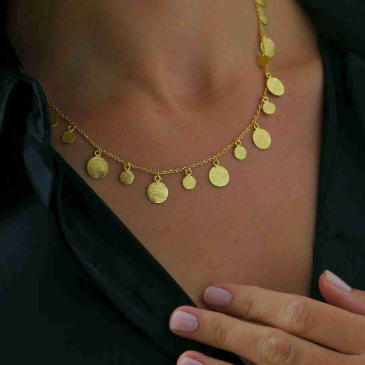 Detailed close-up showing the gold Shimmering Disks Scattered Statement Necklace worn against a black shirt, highlighting the brushed gold discs along the chain.