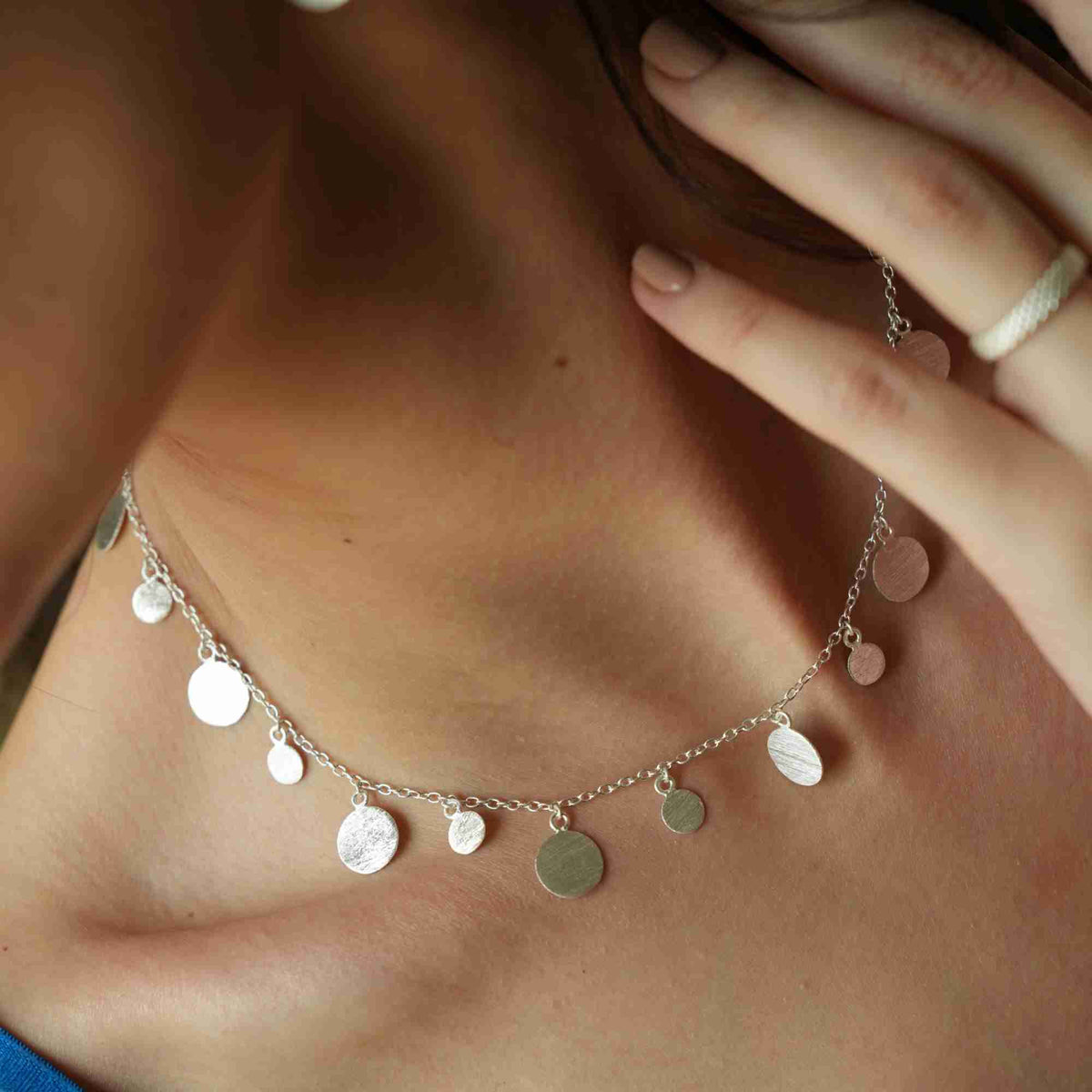 Close-up of scattered disc necklace in silver resting on the collarbone, hand-brushed discs catching the light