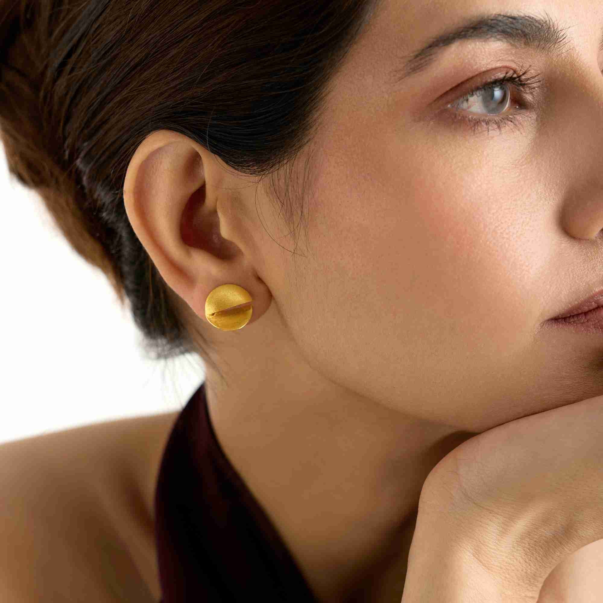 Side profile view of a model wearing the Shimmering Disks Sculptural Disc Stud Earrings in gold, highlighting the folded 3D circular design on the earlobe.
